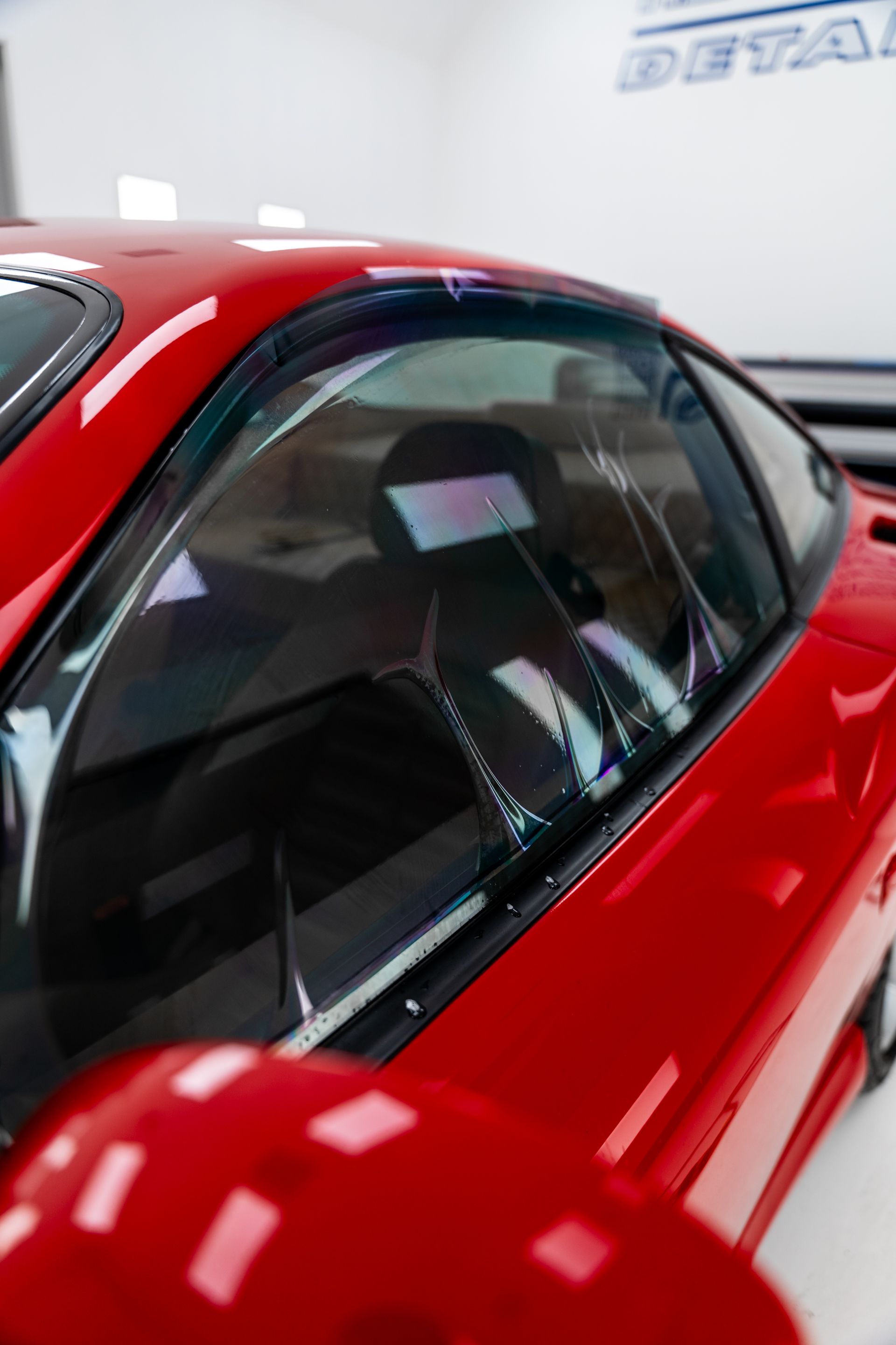 Red sports car with a glossy black-tinted window in a bright showroom