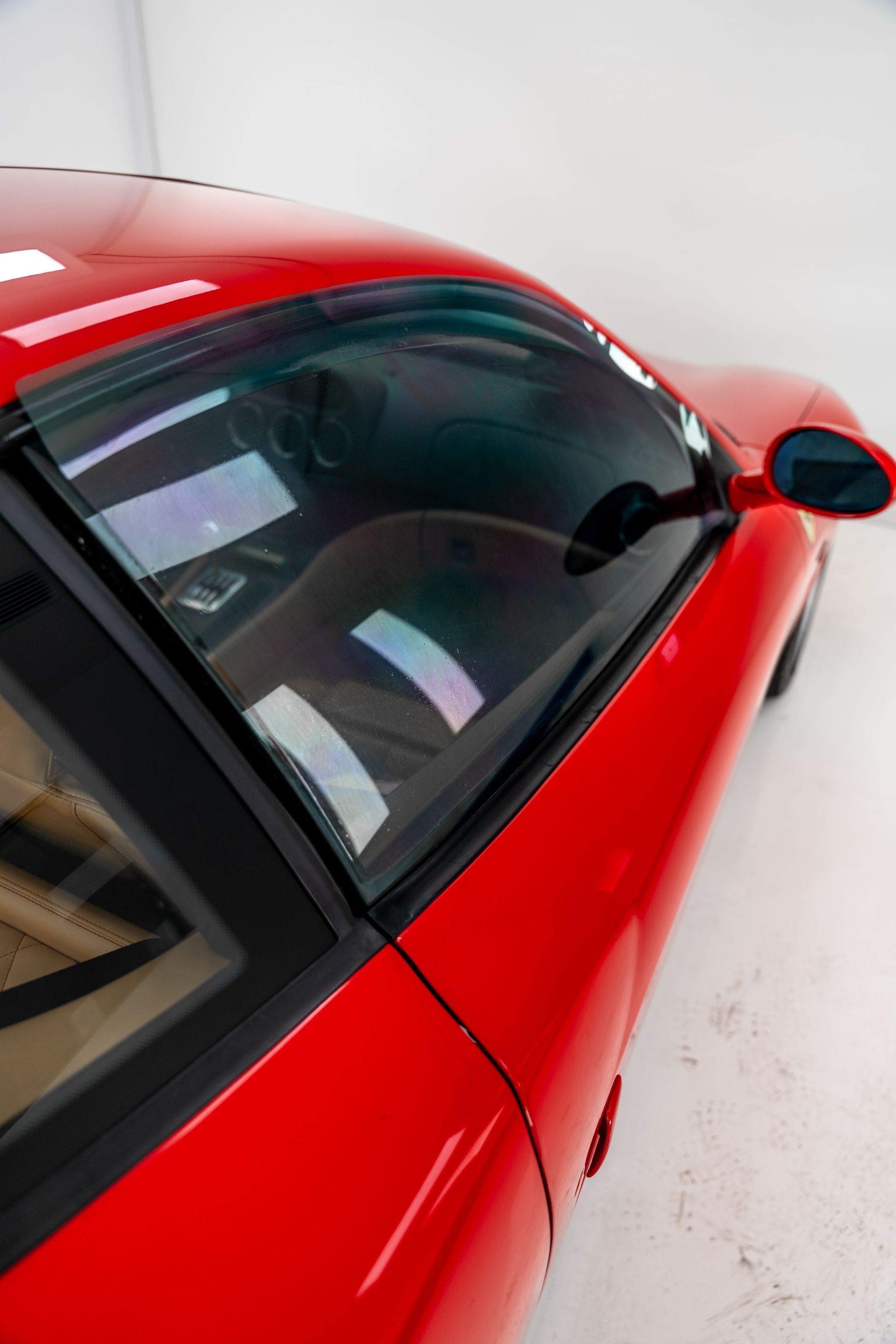Red sports car seen from above, with a black roof and side mirror on a light-colored floor.