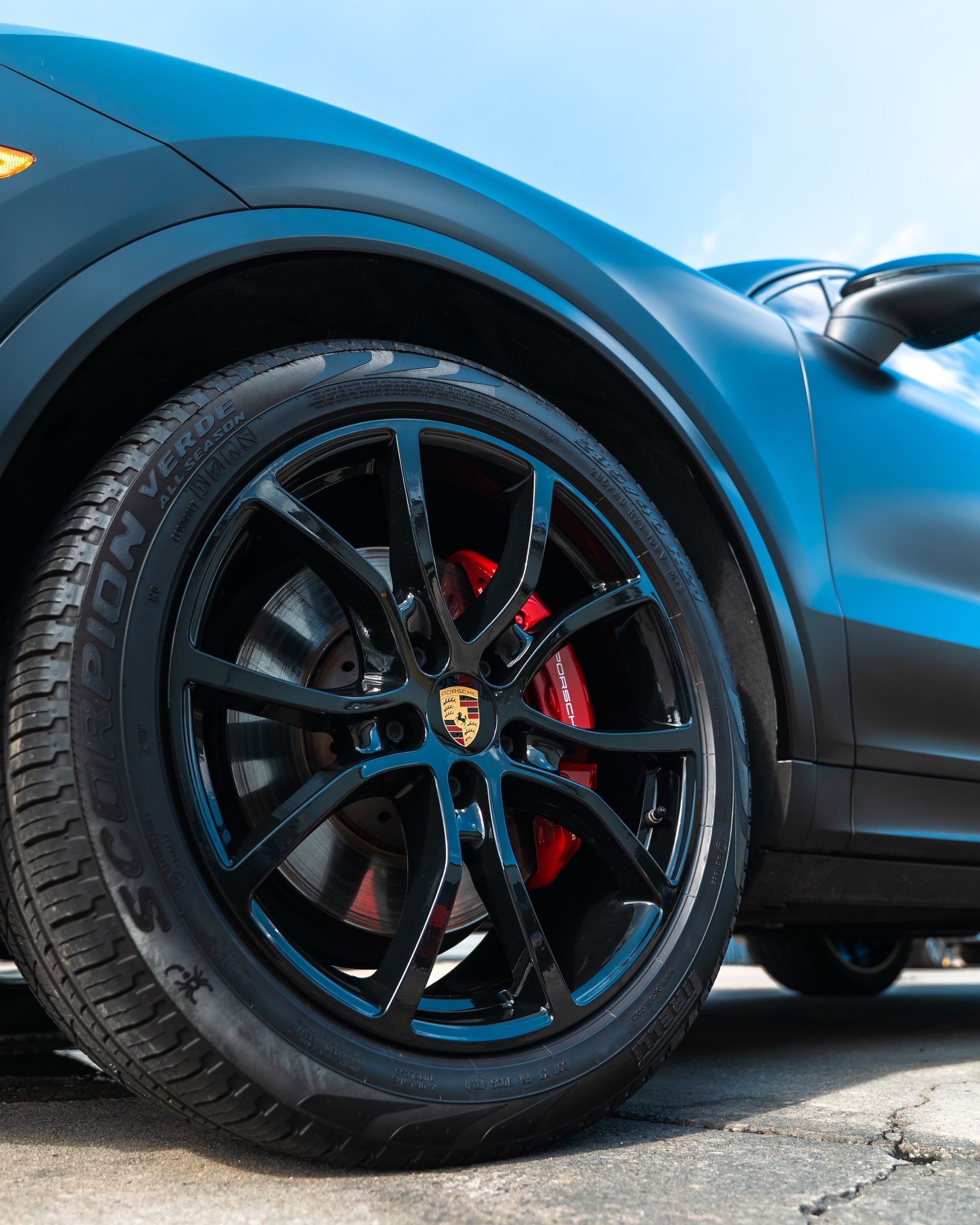 Close-up of a black sports car wheel with red brake caliper on a blue car