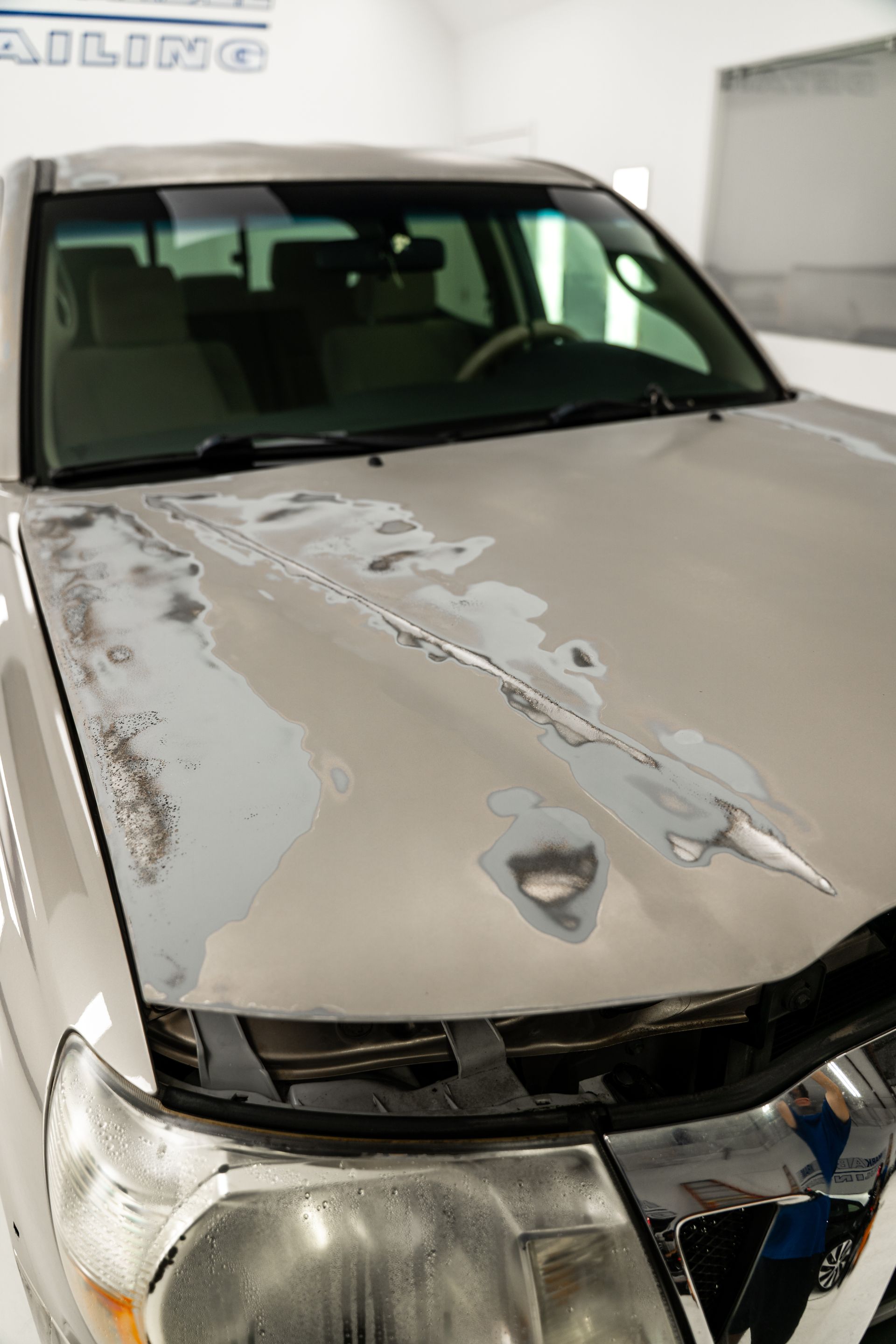 Damaged white SUV with a crushed, peeling hood in a garage