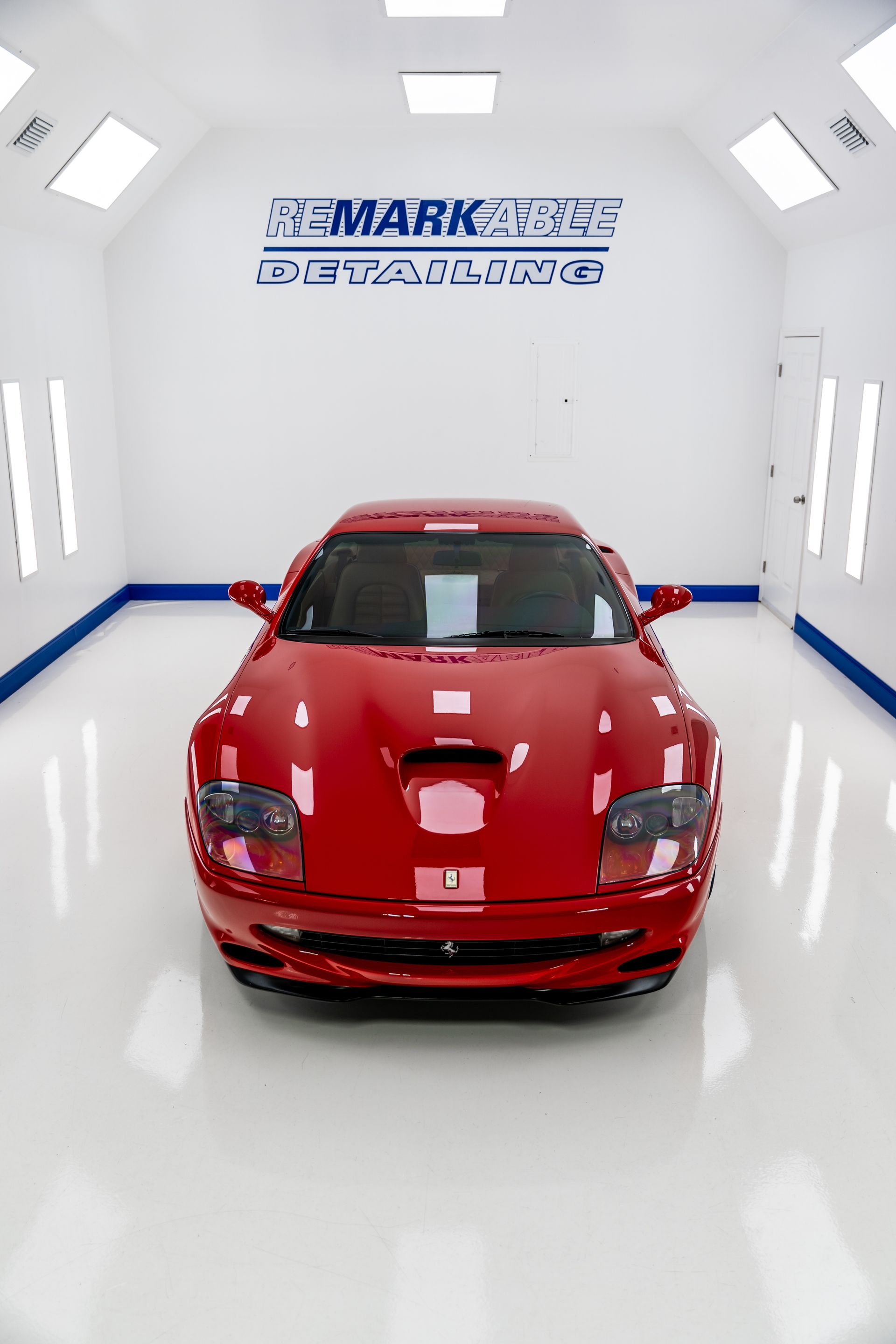 Red sports car centered in a bright white showroom with MARK sign on the back wall