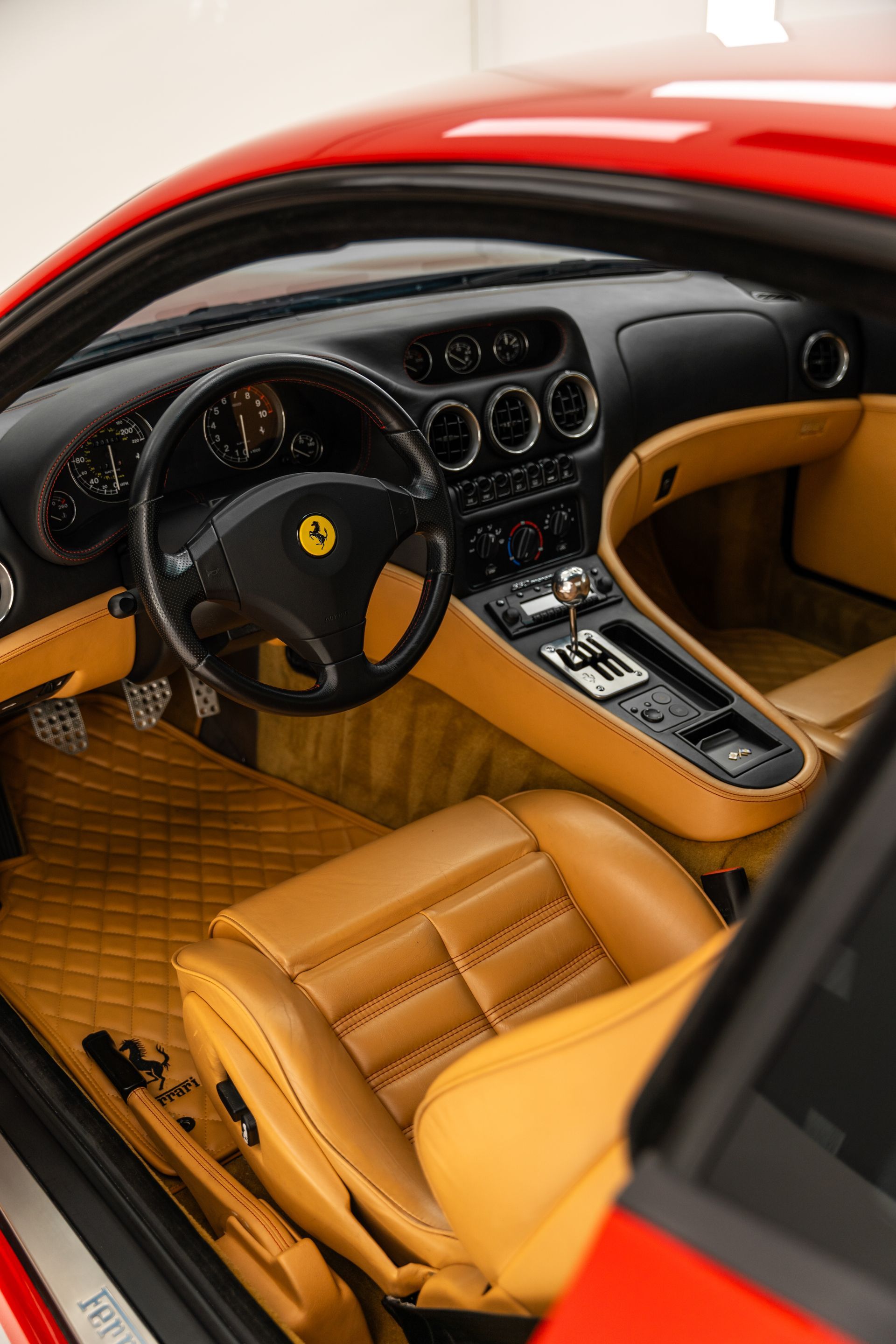 Interior of a red Ferrari with tan leather seats and dashboard, viewed from the open door