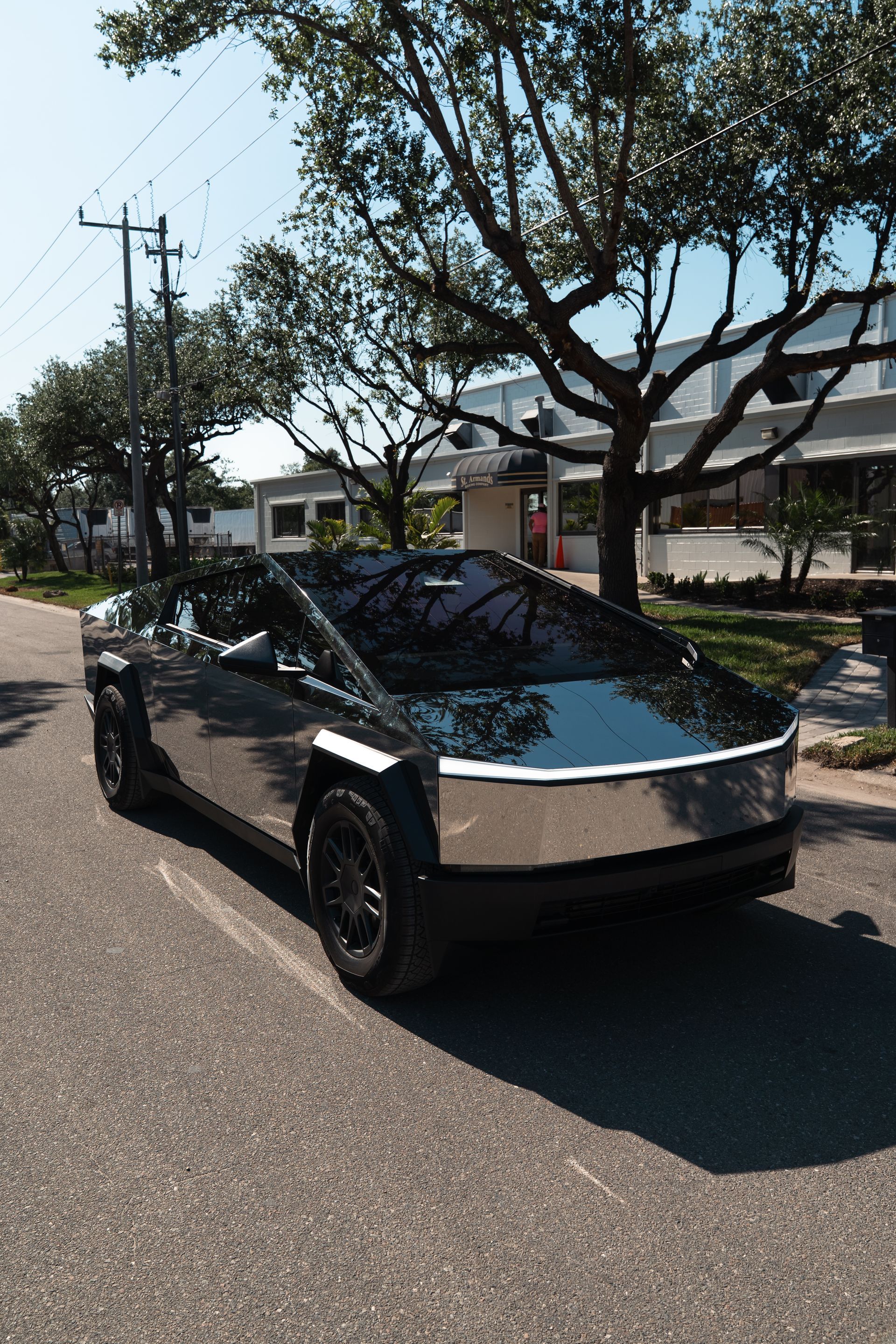 Black Tesla Cybertruck parked on a sunny residential street with trees and houses nearby