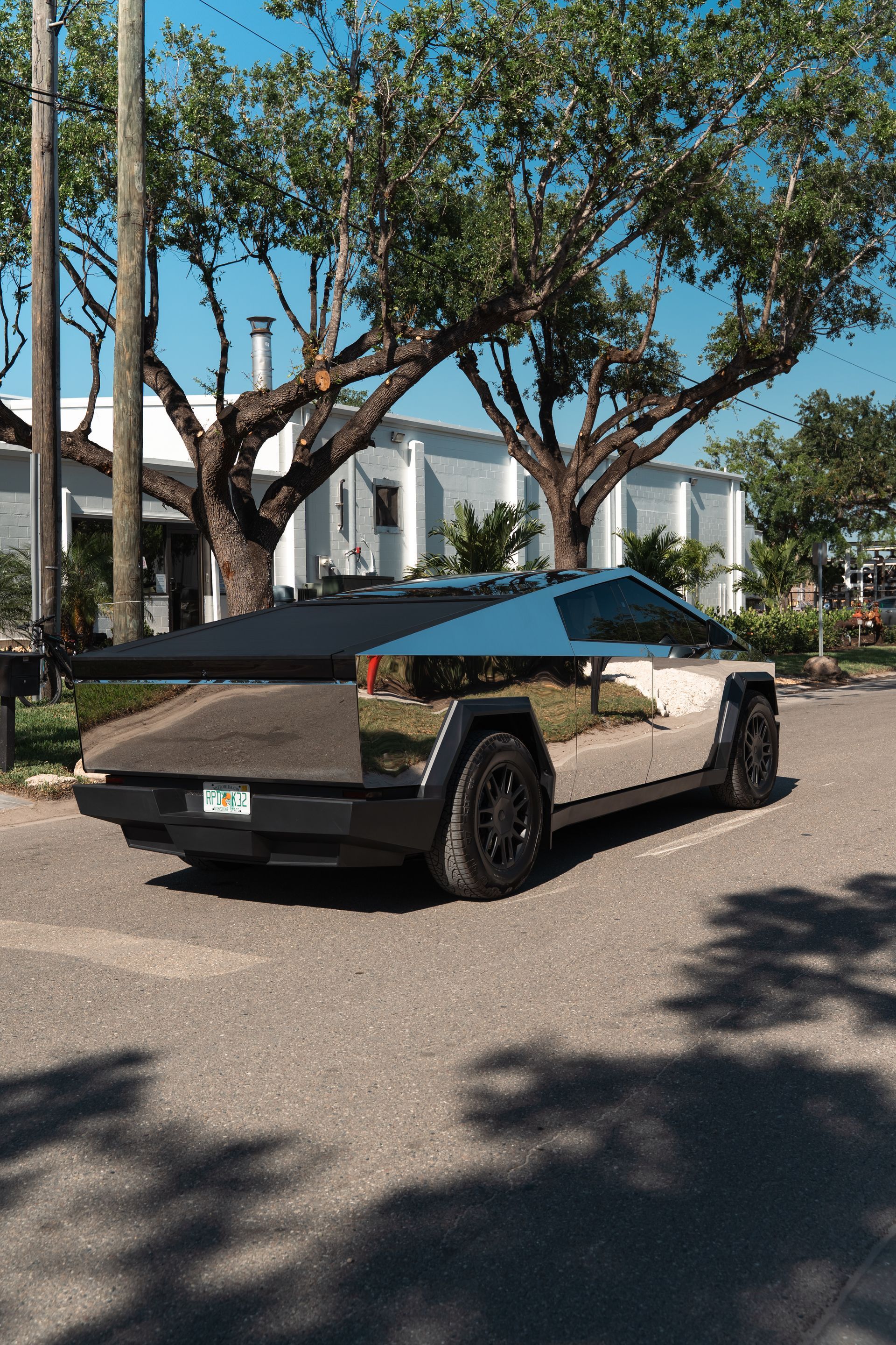 A silver Tesla Cybertruck parked on a sunny street under trees.
