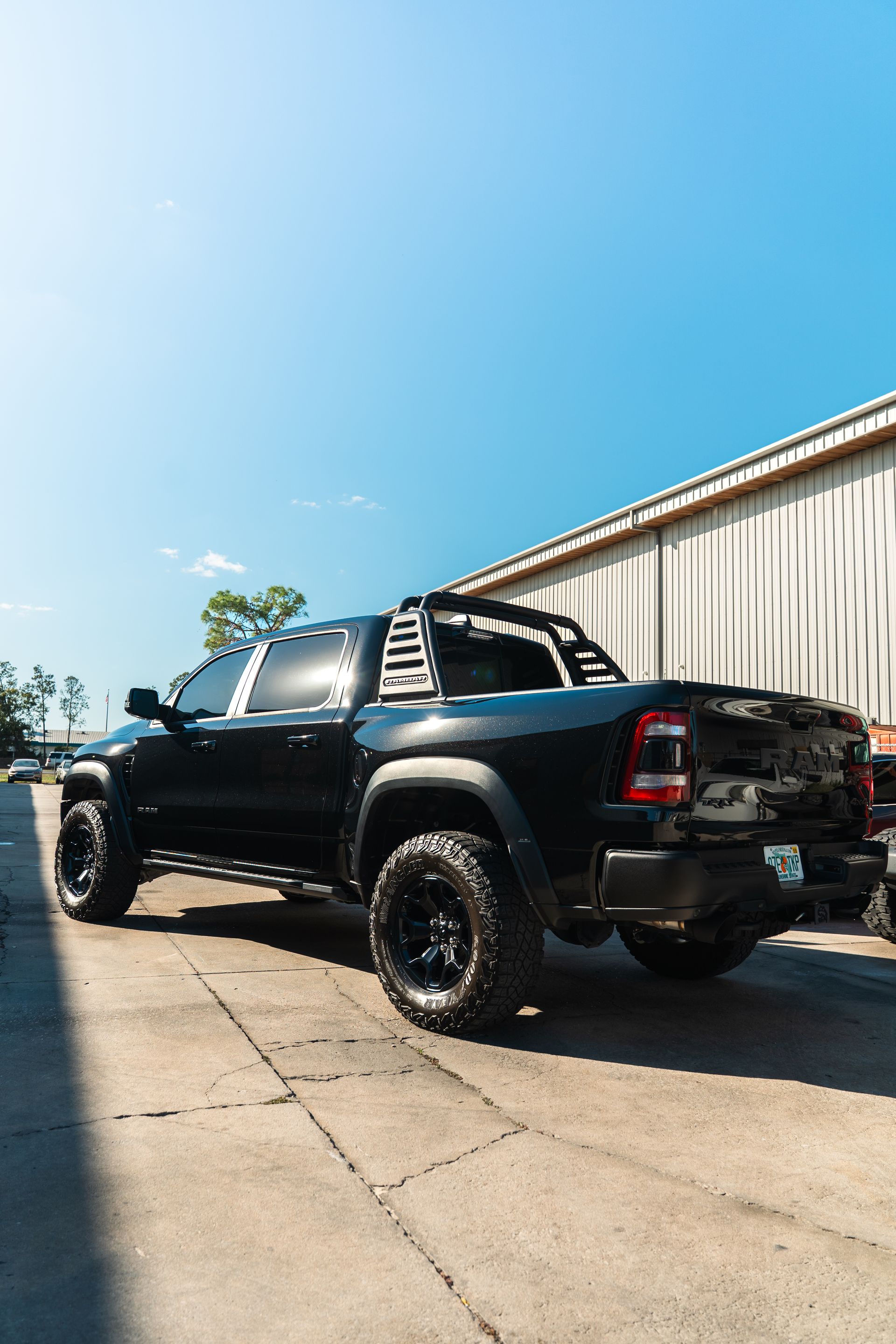 Black lifted pickup truck parked beside a warehouse under a bright blue sky
