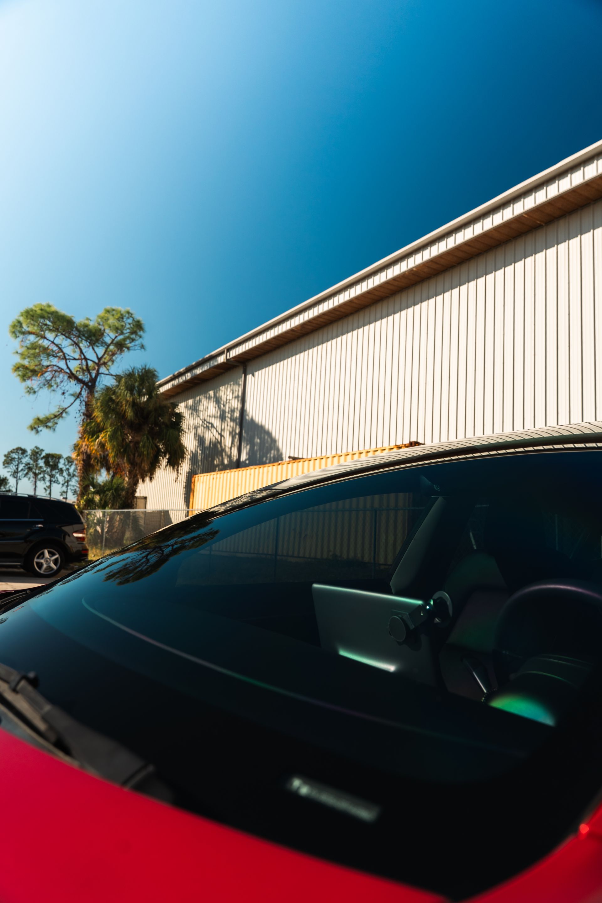 Red car parked beside a beige building under a clear blue sky