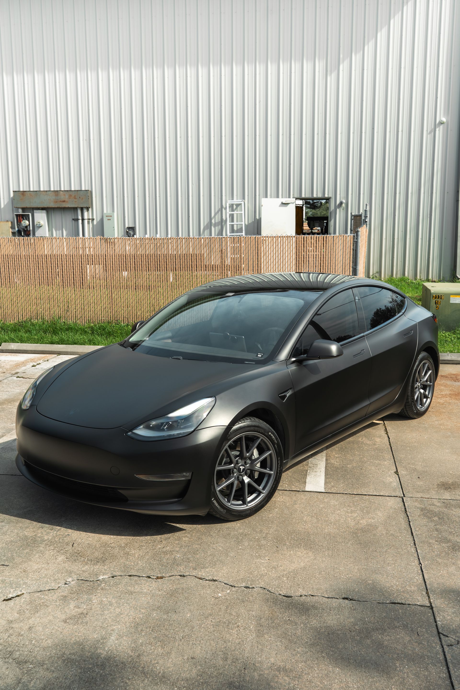Matte black sports coupe parked beside an industrial building