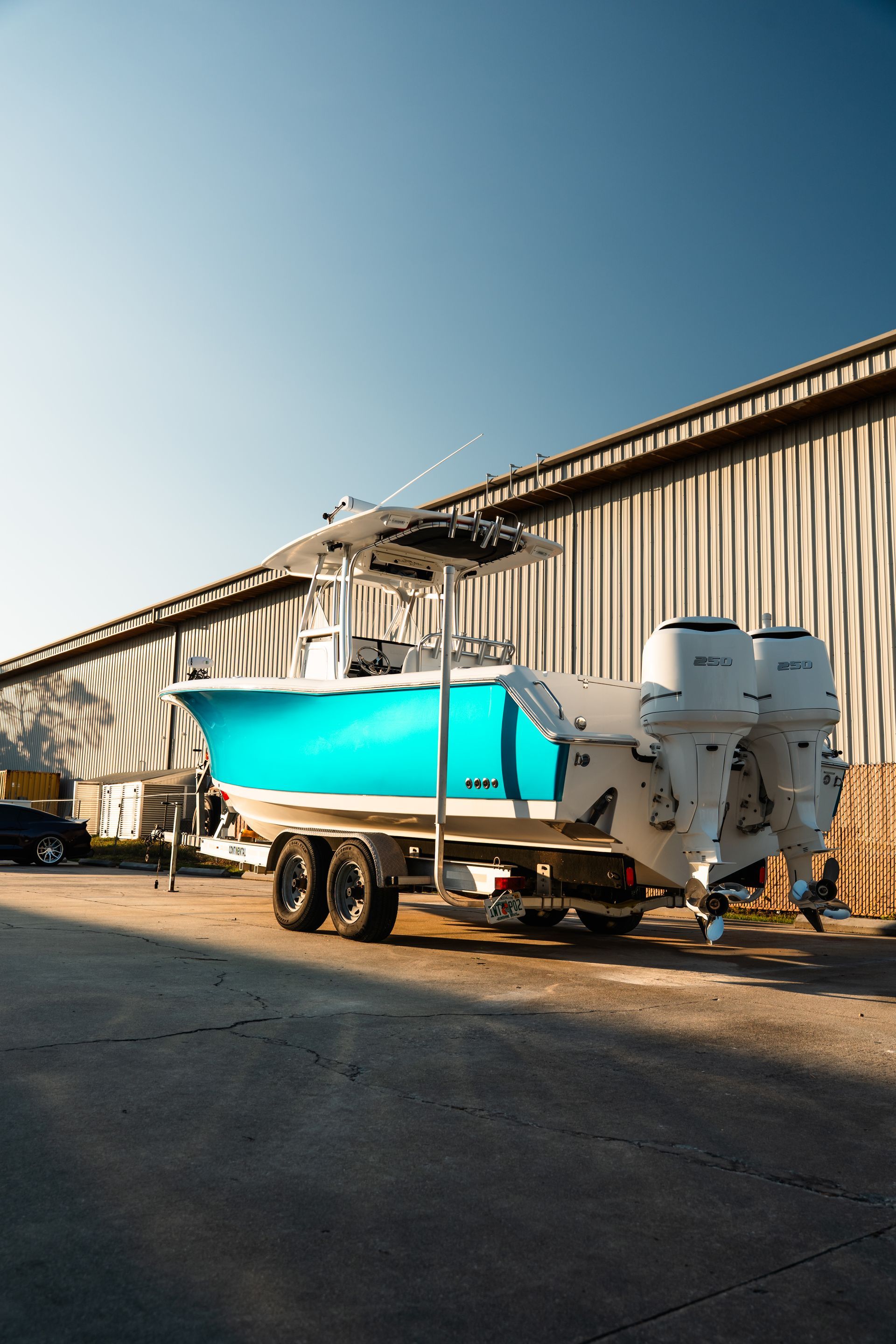 Bright turquoise boat on trailer beside a metal warehouse in late afternoon light