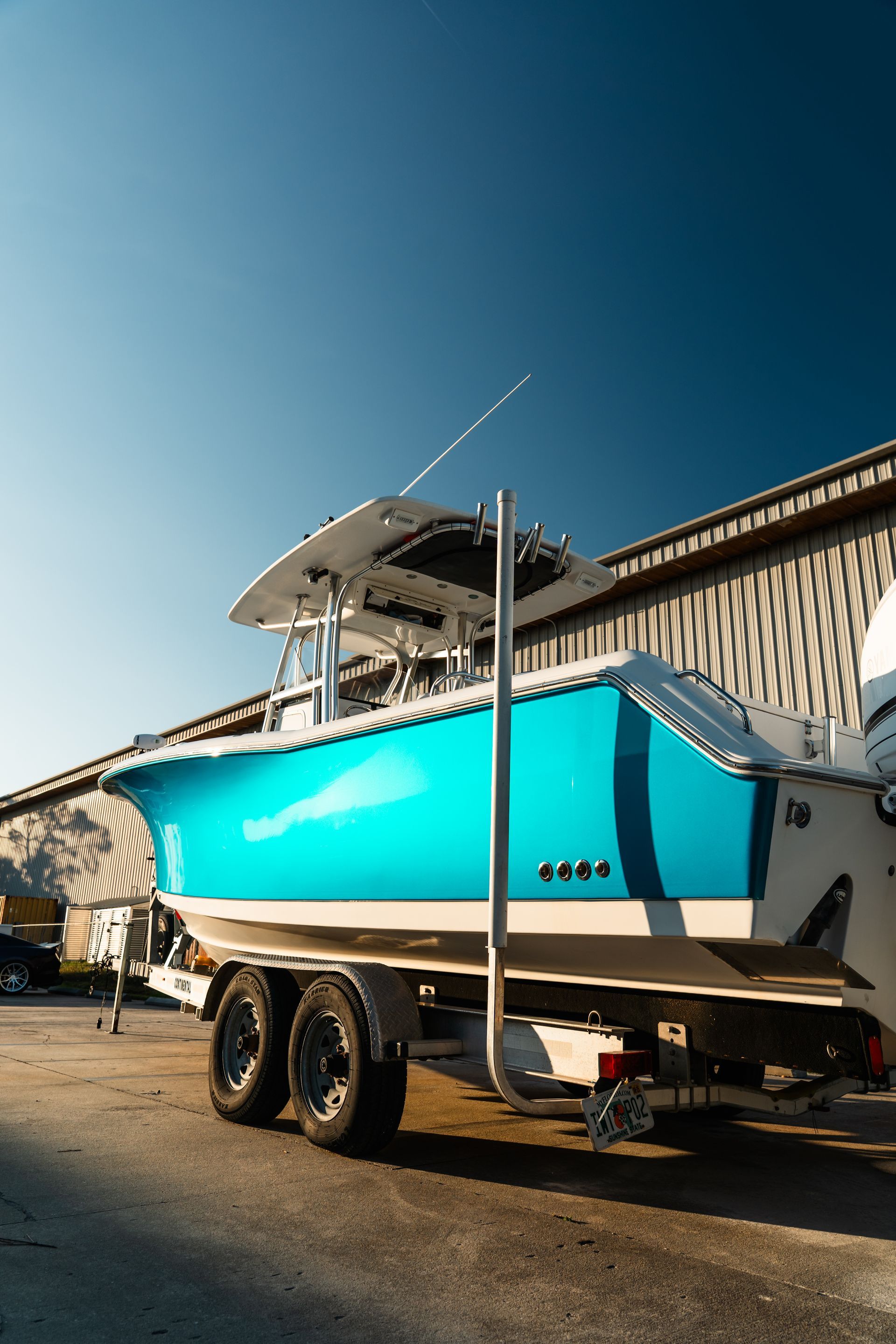 Turquoise center-console boat on a trailer beside a warehouse under a clear blue sky