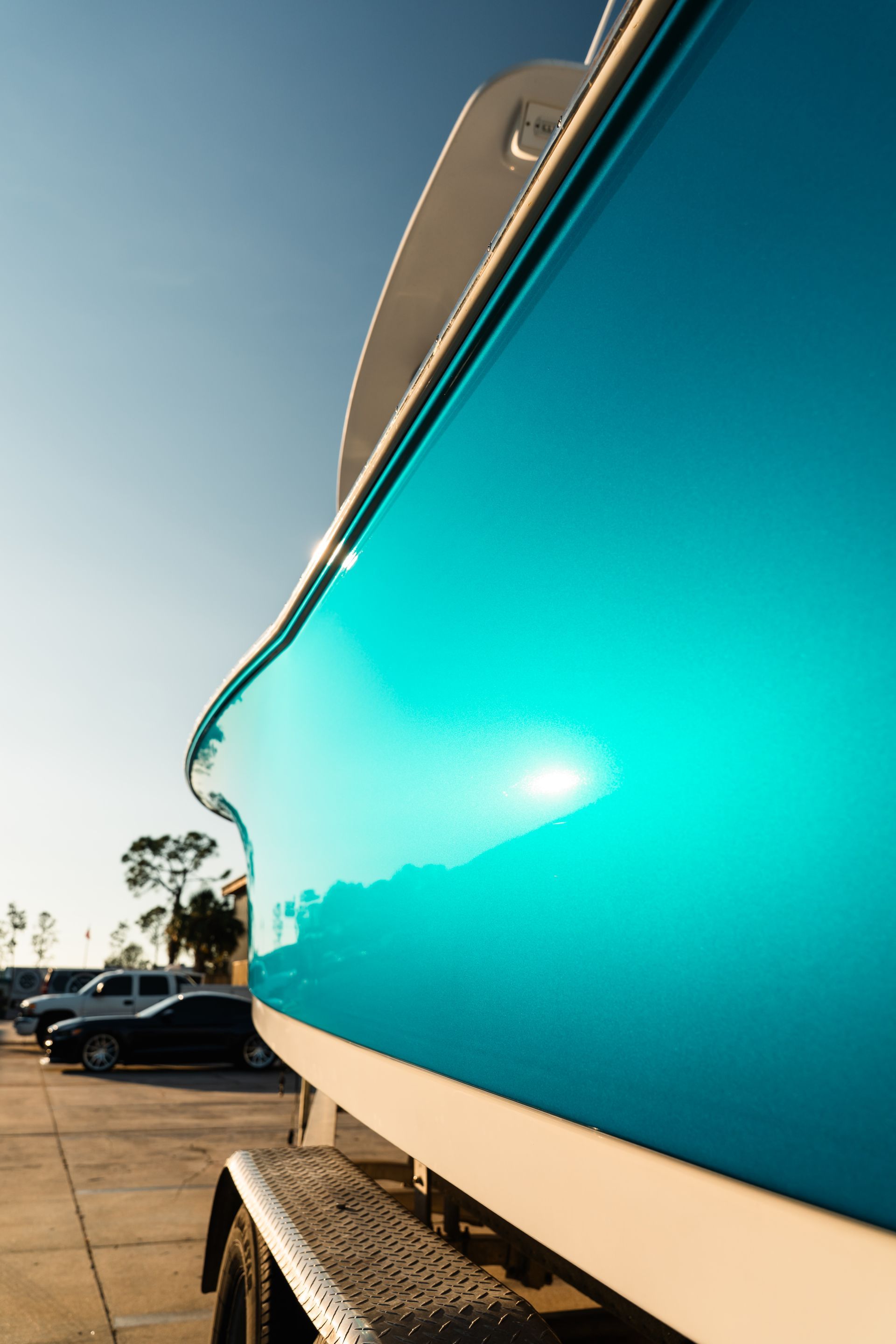 Close-up of a turquoise boat hull on a trailer in a sunny parking lot