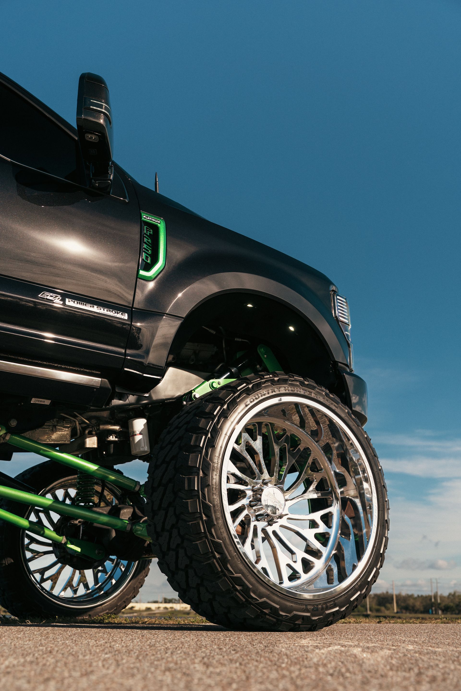 Lifted black truck with large chrome wheels on a road under a blue sky