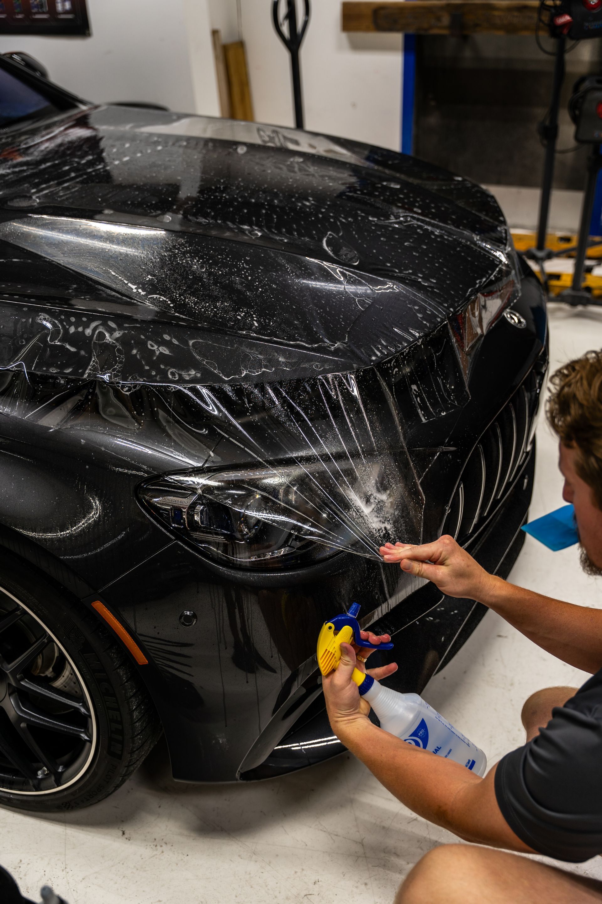 Person washing the front of a black car with a spray bottle in a garage