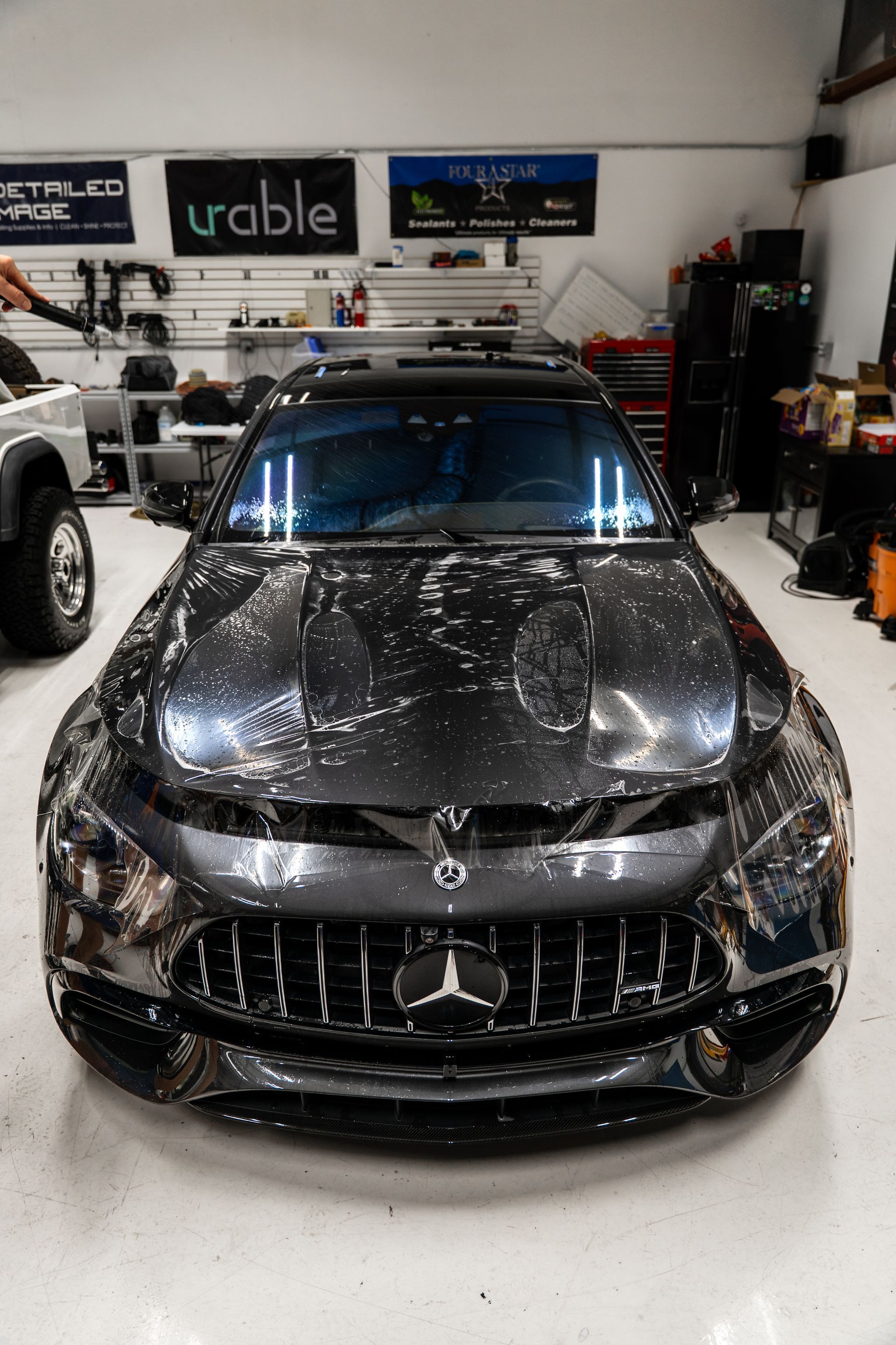 Black luxury sports car covered in cracked white pattern, parked in an auto shop garage