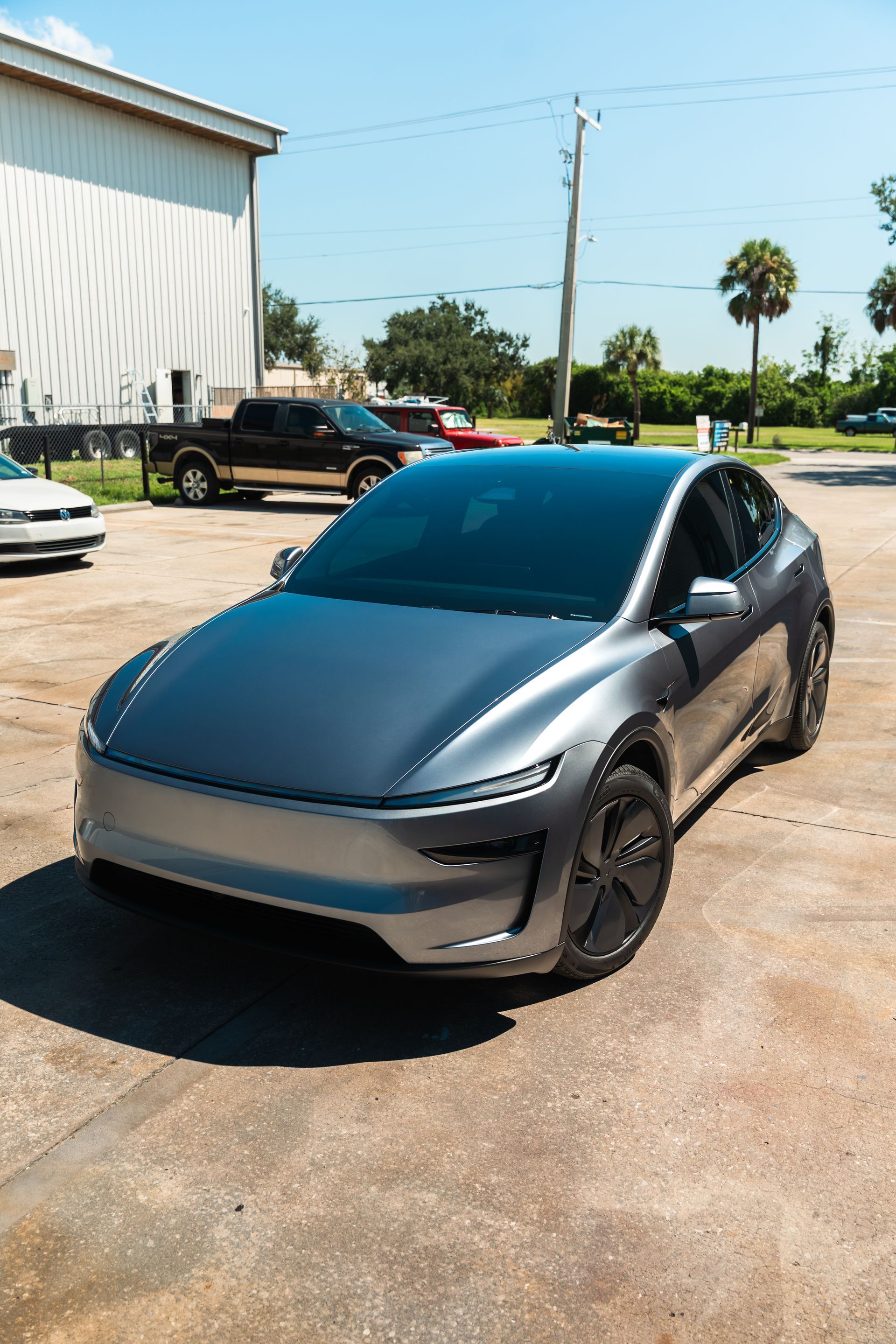 Gray Tesla sedan parked outdoors beside a white building on a sunny day