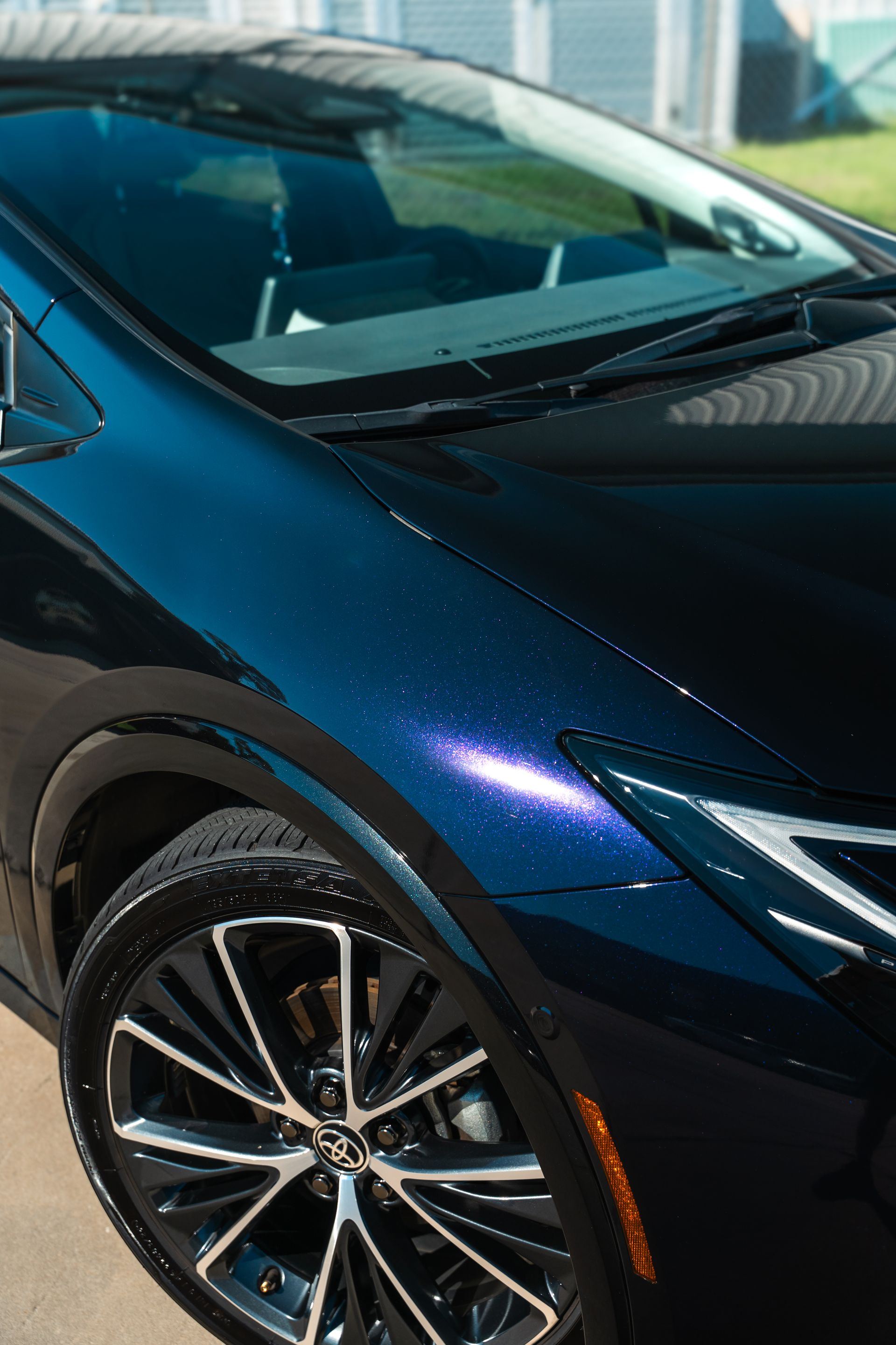 Close-up of a blue and black car’s front side and wheel, parked outdoors