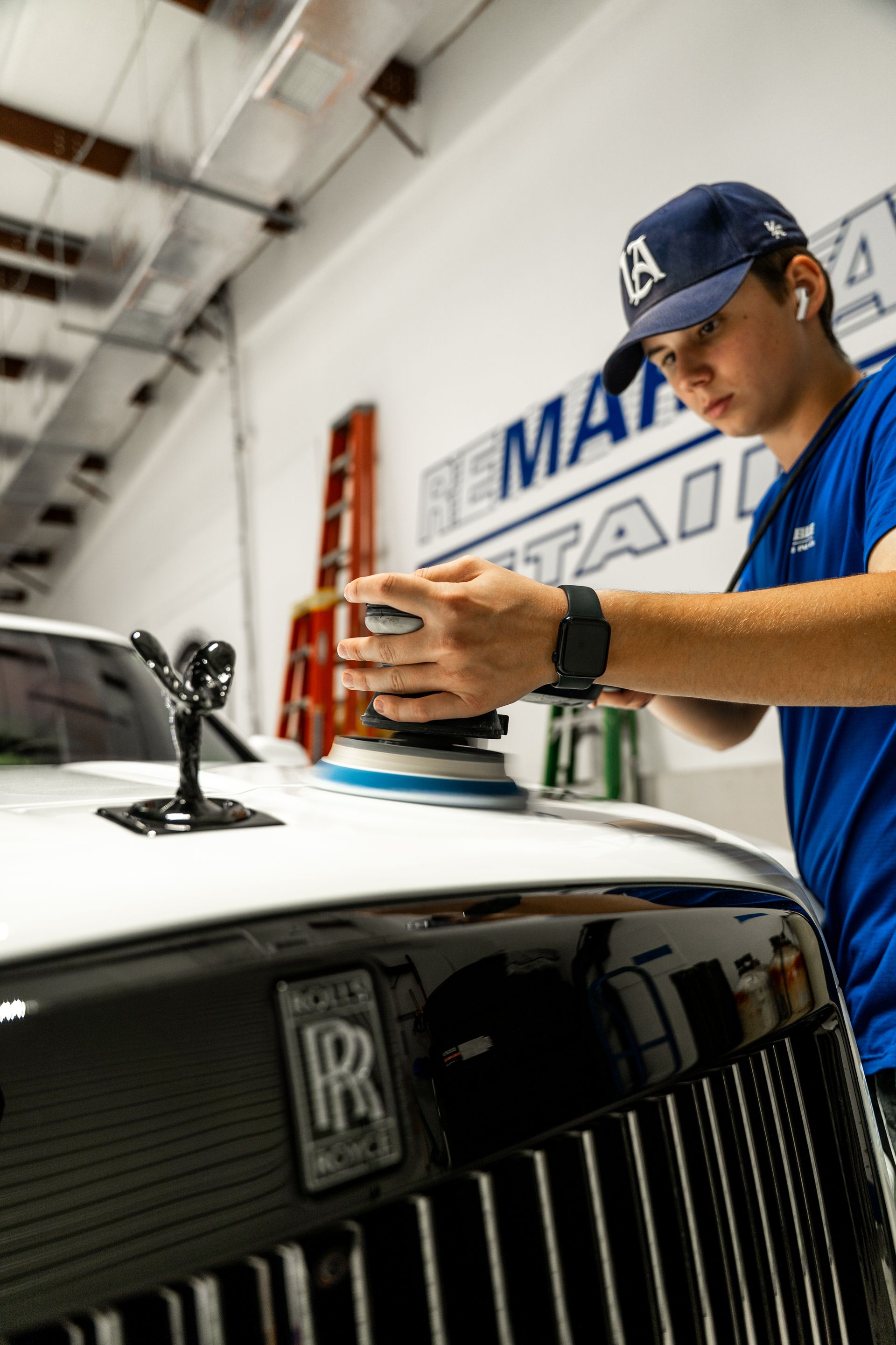 Mechanic working on a white Rolls-Royce in a garage, with the hood ornament and grille in view
