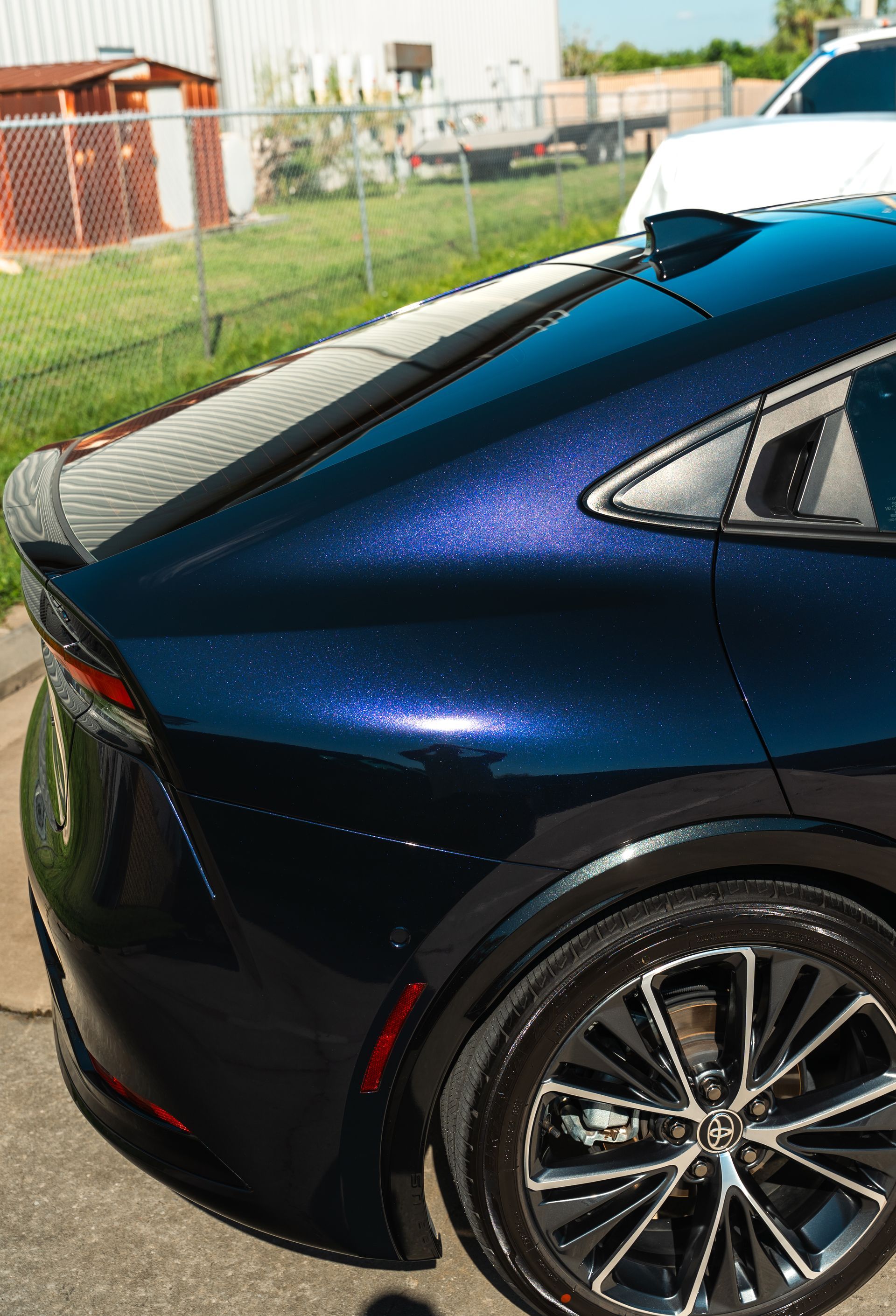 Rear side view of a dark blue sedan with a black roof, parked beside a fence.