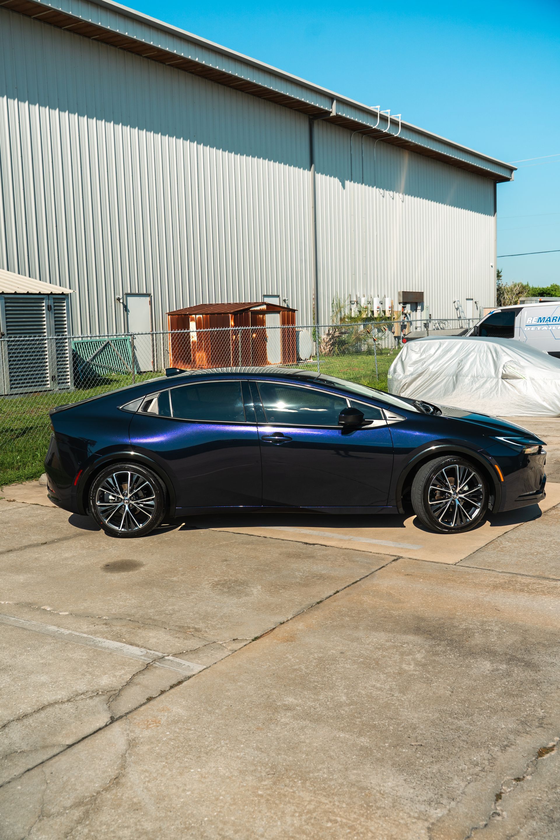 Dark blue sedan parked beside a white industrial building on a sunny day