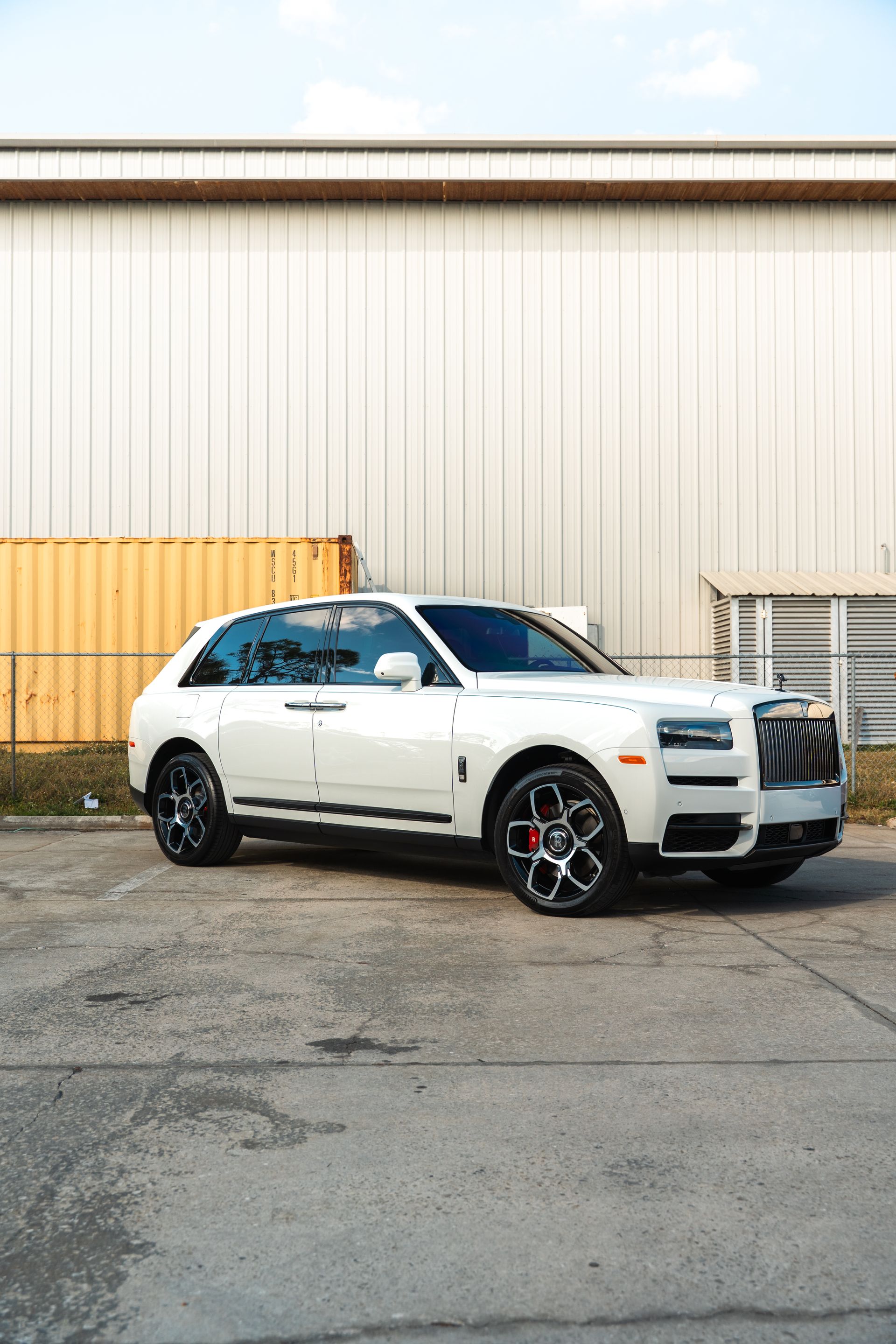 White SUV parked outside an industrial building with a beige metal wall and cracked pavement
