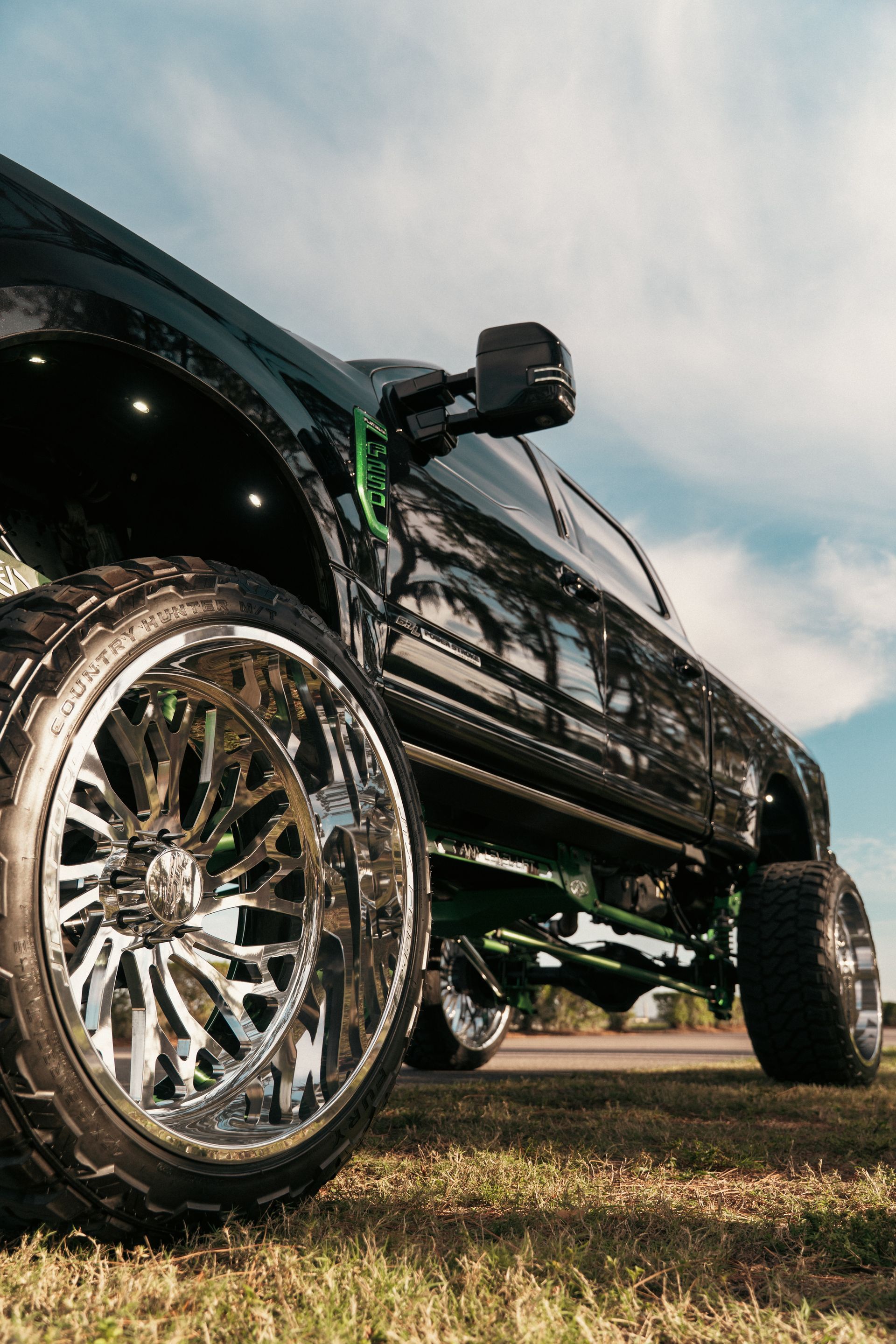 Lifted black truck with chrome wheels parked on grass under a cloudy sky