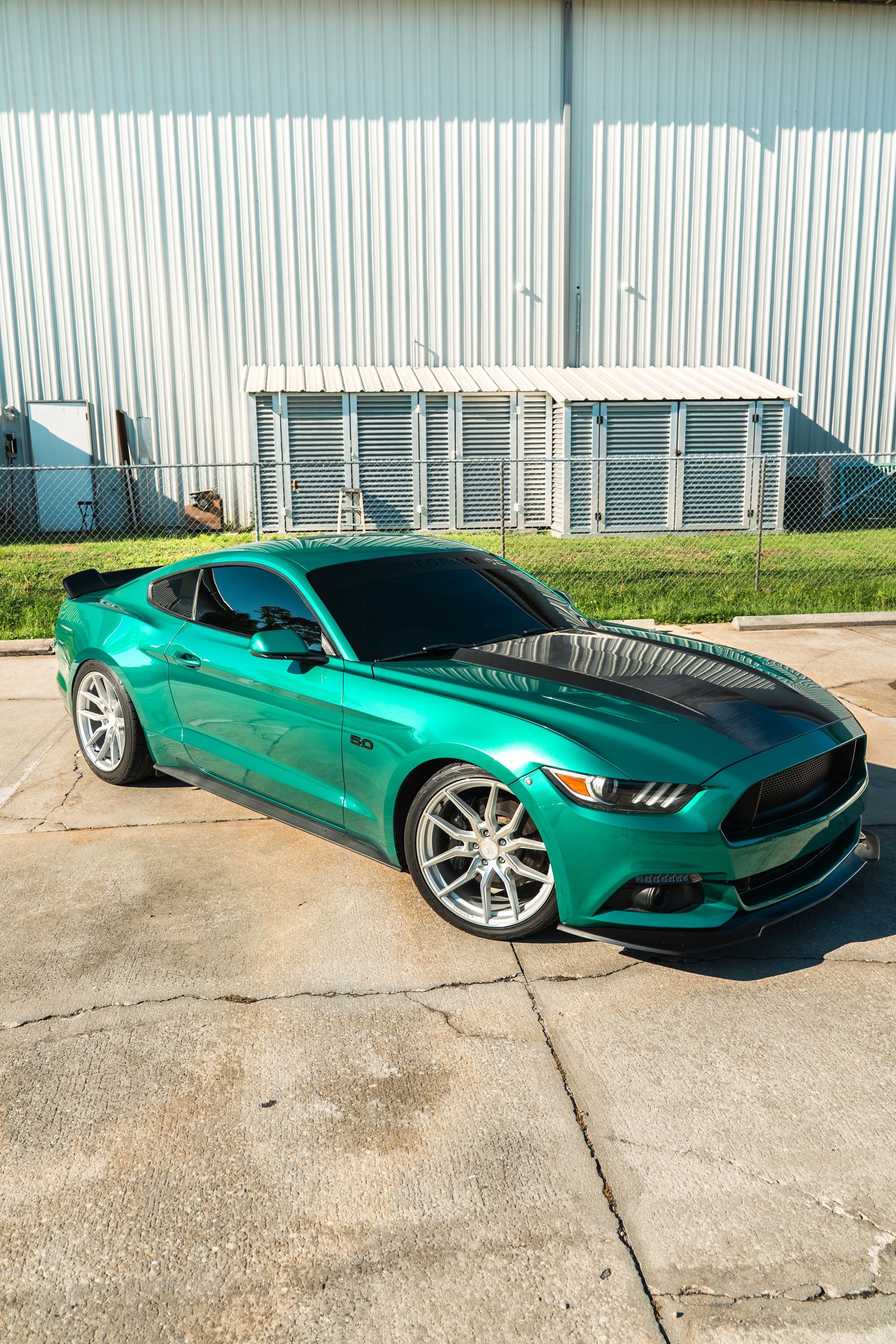 Green sports car parked outside a metal building