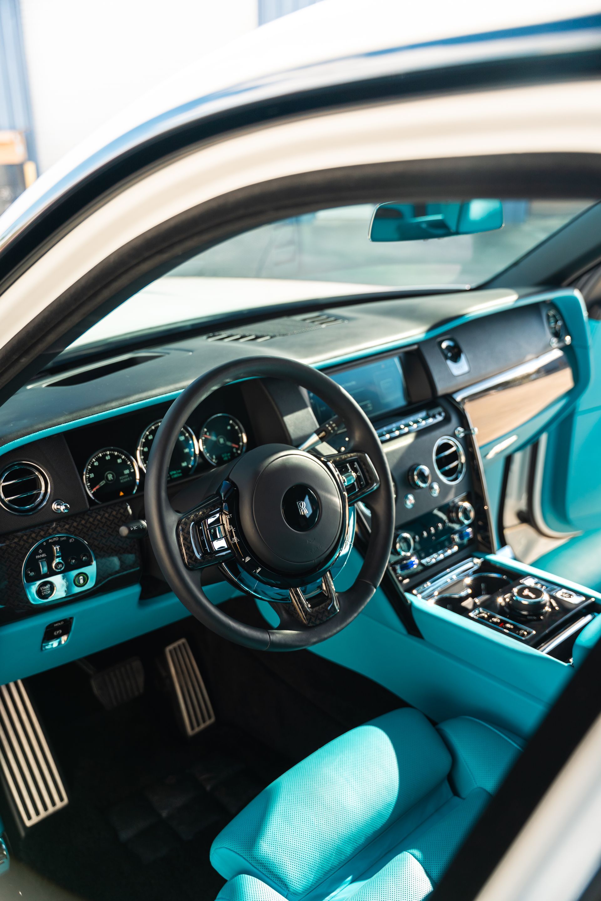 Luxury car interior with turquoise seats, black dashboard, and steering wheel seen through the open door