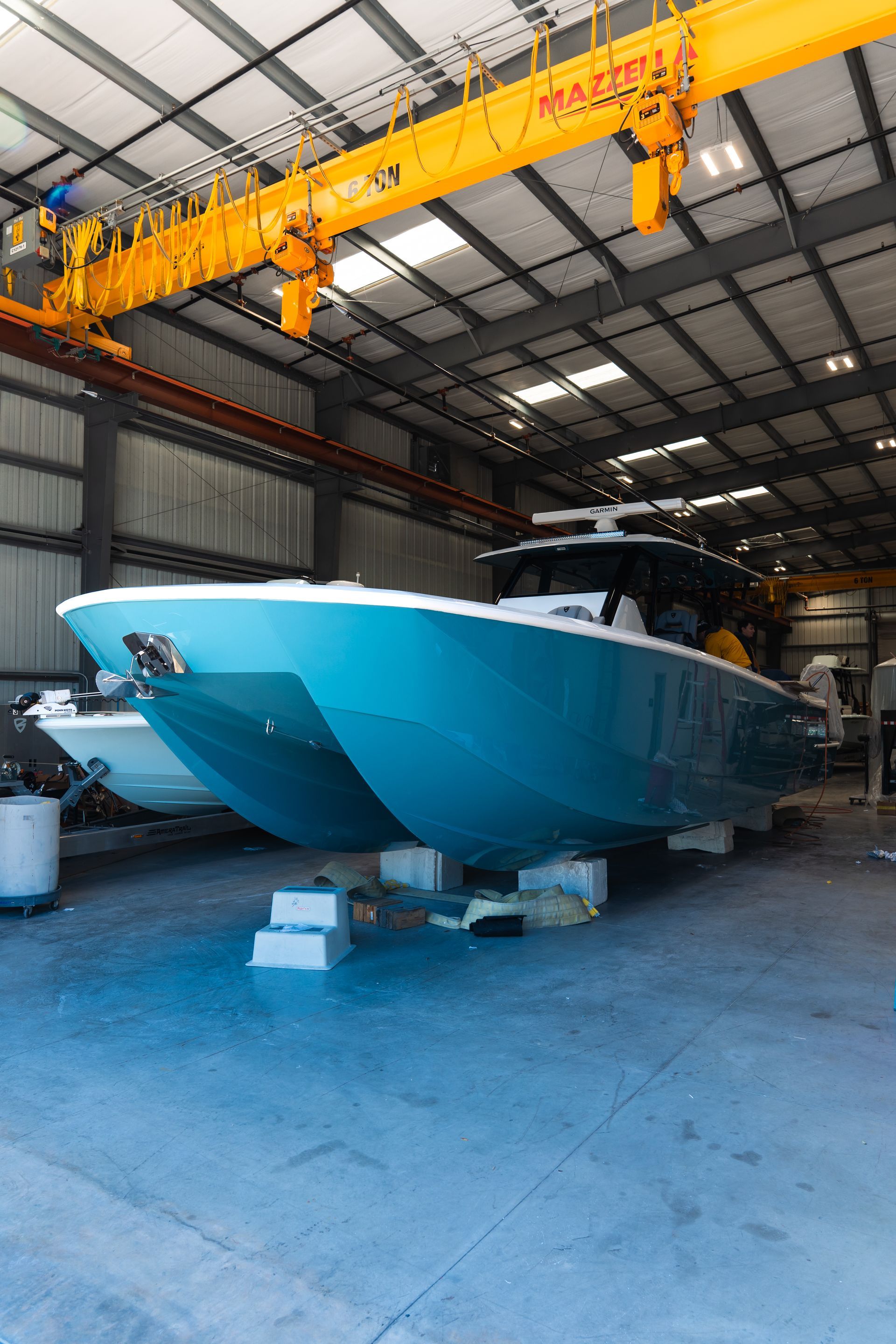 Blue motorboat in a warehouse under a yellow overhead crane, sitting on blocks.