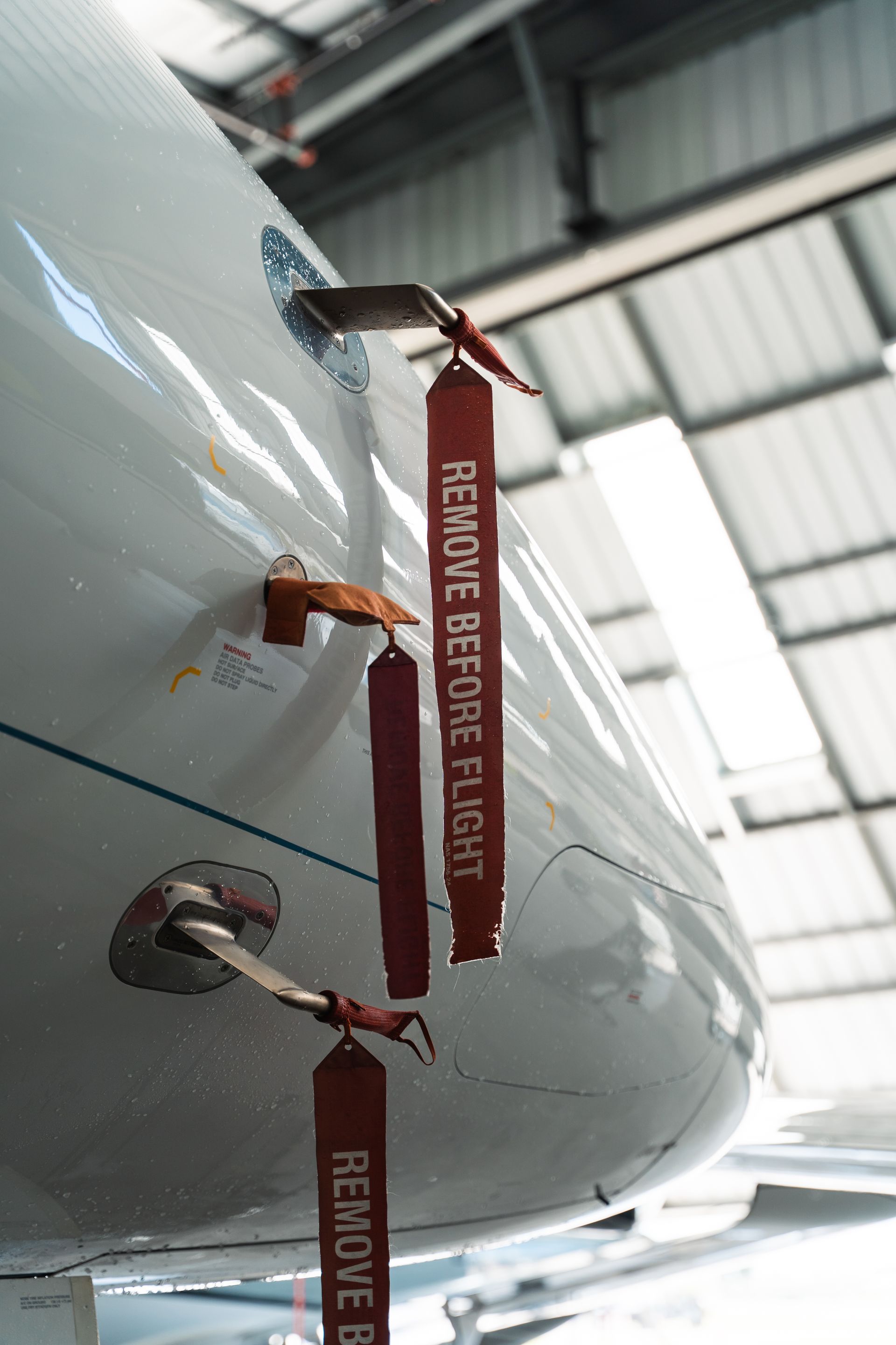 Red “REMOVE BEFORE FLIGHT” tags hanging from a white aircraft in a hangar