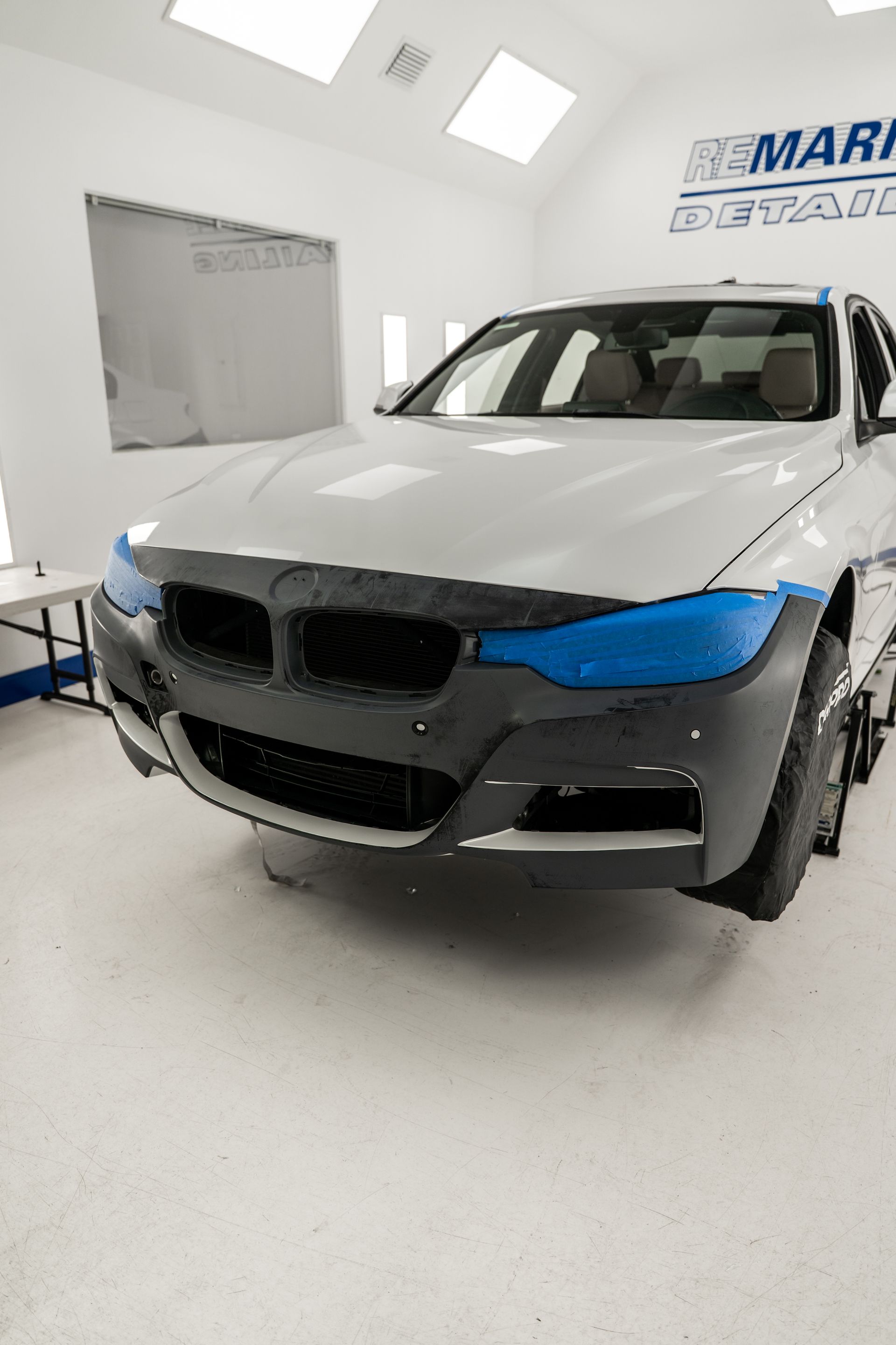 Front view of a white BMW SUV with blue accents in a bright auto body shop