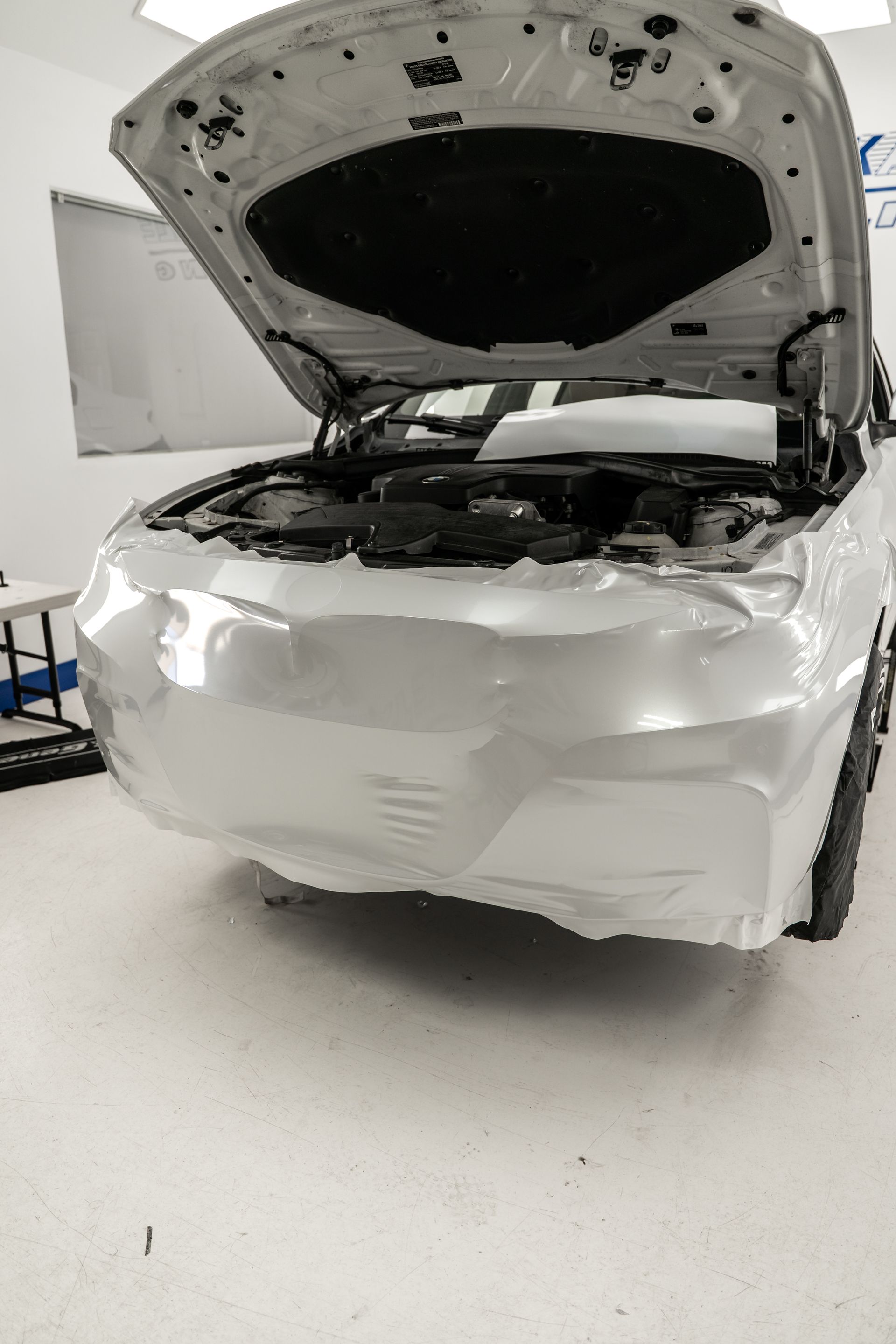 White car with hood open, showing front-end damage in a workshop
