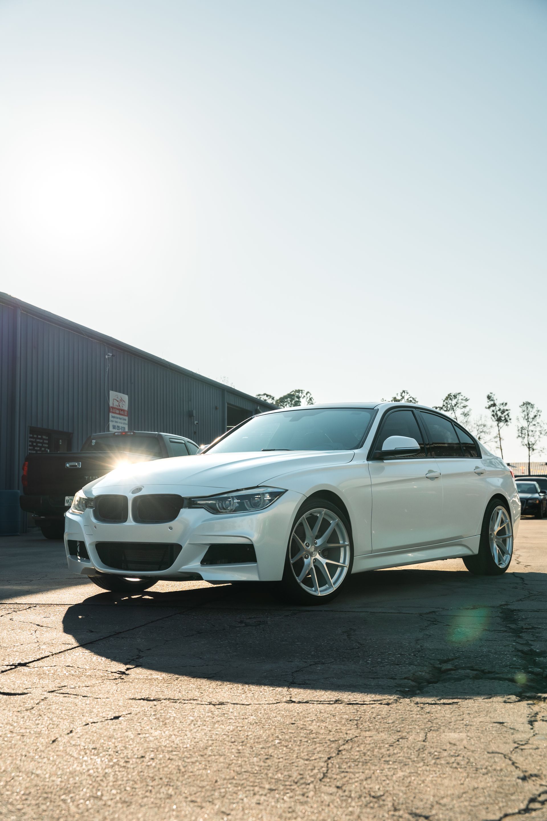 White sedan parked outdoors by a warehouse, low-angle view in bright sunlight