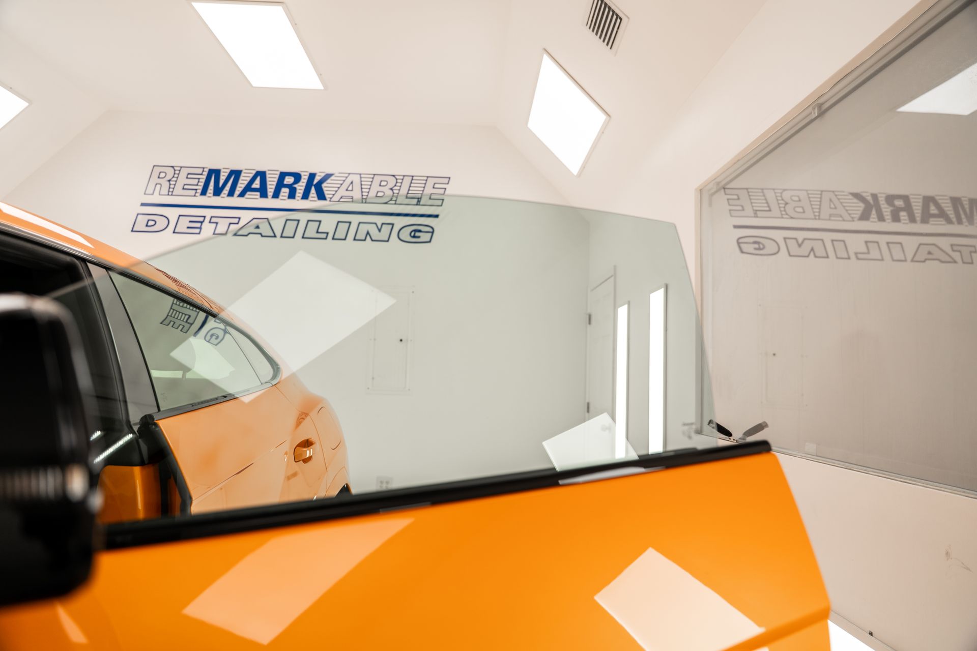 Orange car in a bright auto shop with a large windshield and wall signs reading “MARK” and “TEXACO”
