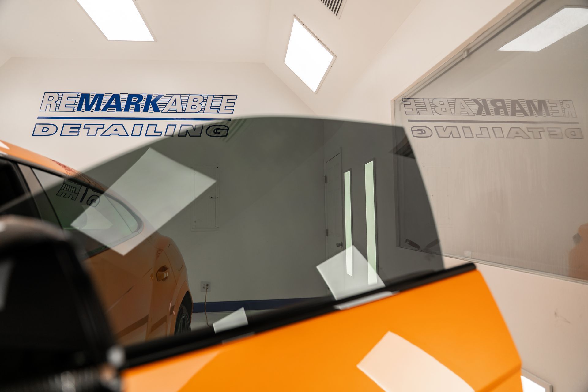 Orange car windshield being installed in a workshop, with protective film and branding in the background.