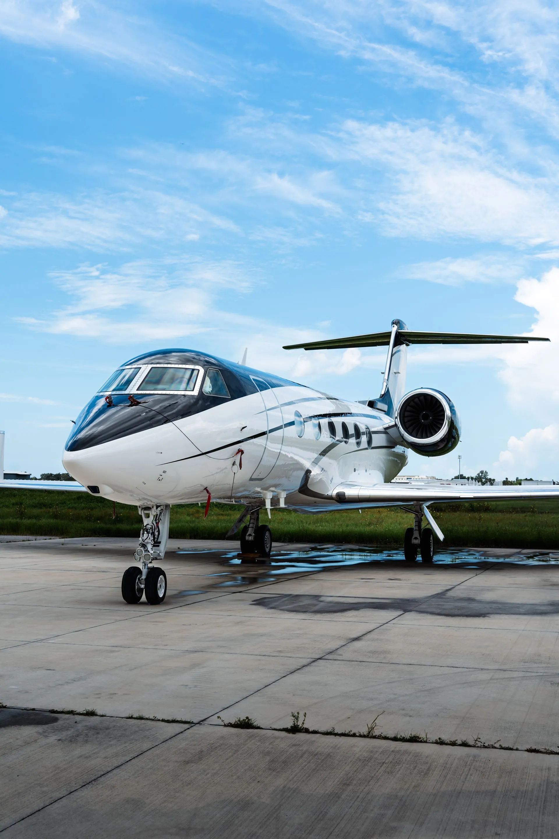 Small white jet parked on tarmac under a blue sky, viewed from the front-left side.
