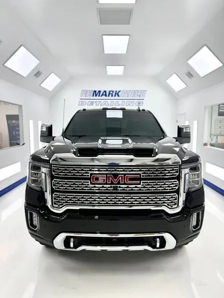 Black GMC pickup truck in a bright showroom, front view, with a “MARK” sign in the background