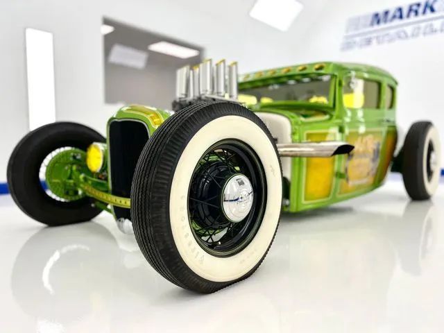 Green custom hot rod with whitewall tires on a glossy white floor, shown in a studio setting