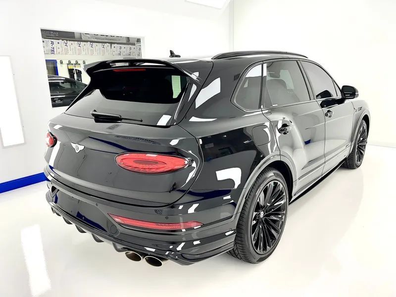 Black SUV in a bright showroom, rear three-quarter view with tinted windows and black wheels