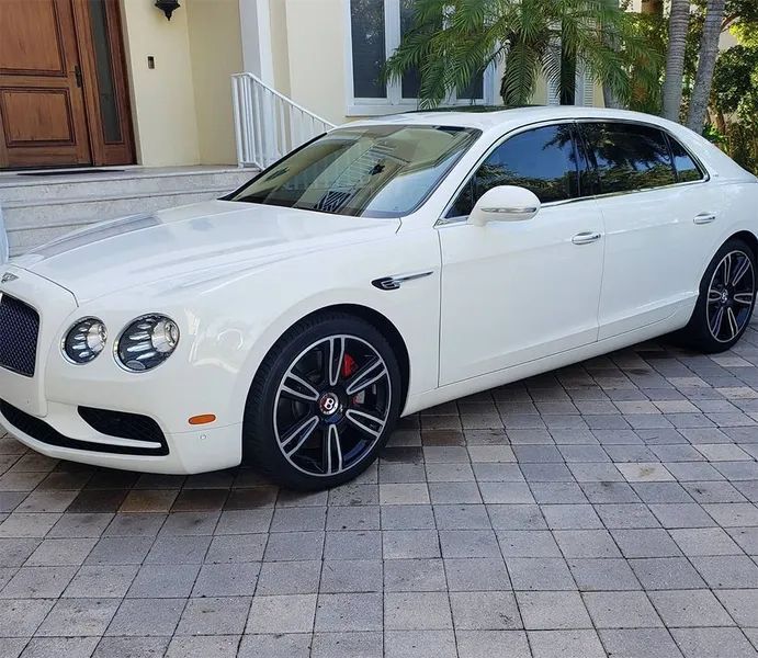 White luxury sedan parked on a driveway outside a house with palm trees