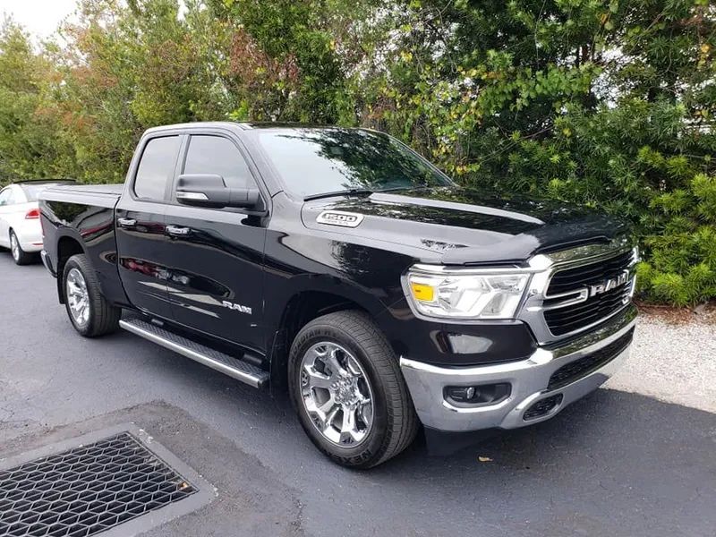Black pickup truck parked on a street beside greenery and a white car