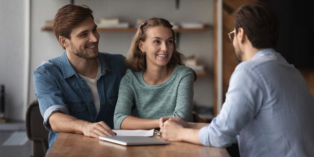 A man and a woman are sitting at a table talking to a man.