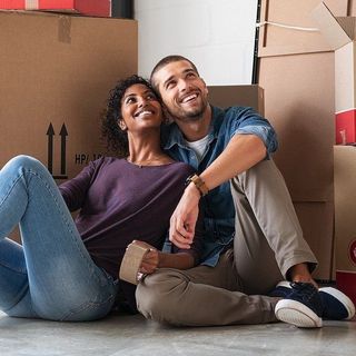 A man and a woman are sitting on the floor in front of cardboard boxes.