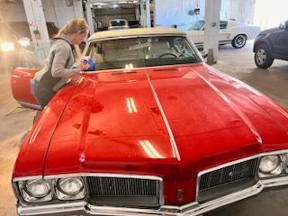 A woman is standing next to a red car in a garage.