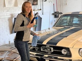 A woman is standing next to a mustang in a garage.
