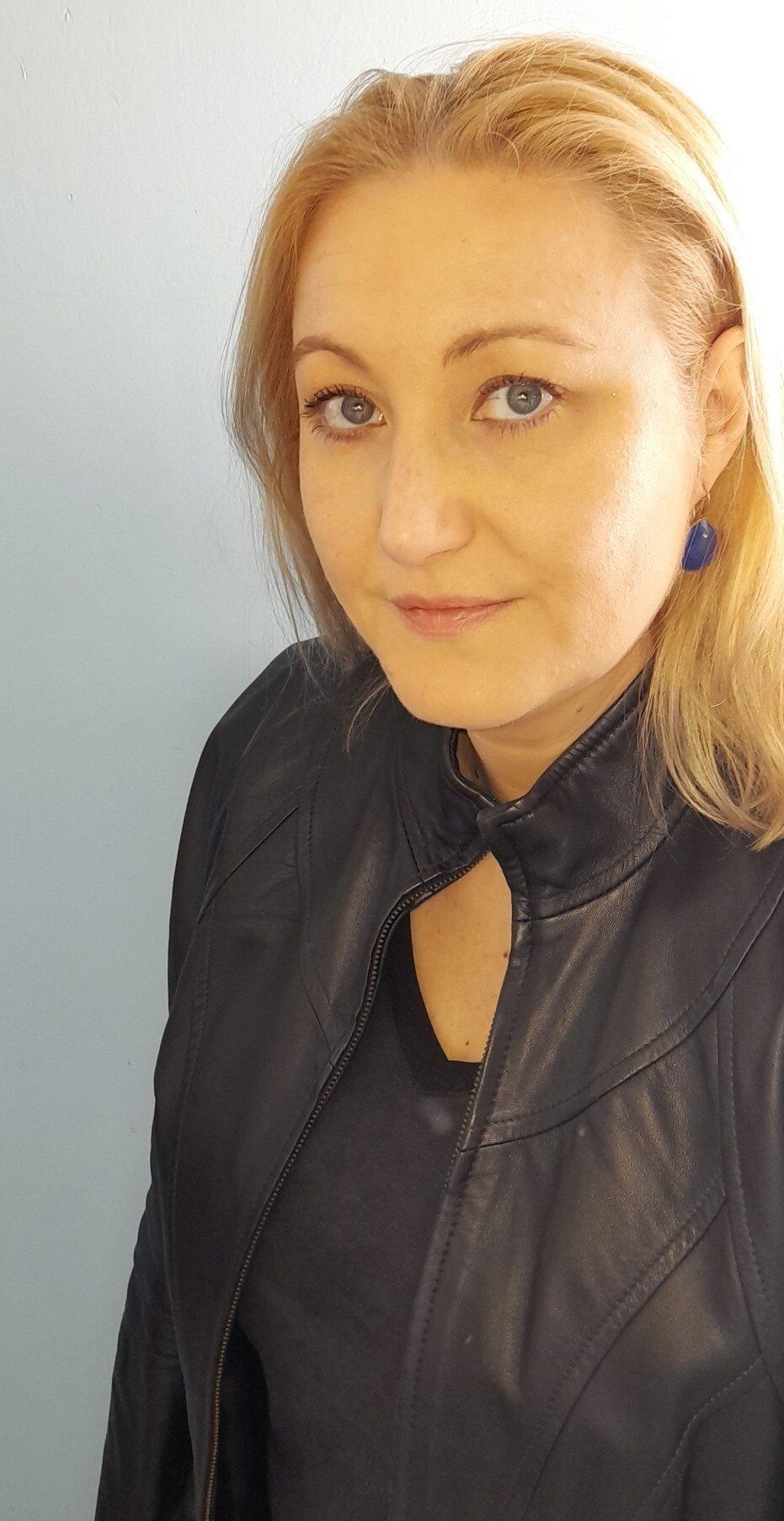 Portret van een blonde persoon in een zwarte leren jas tegen een lichte achtergrond.