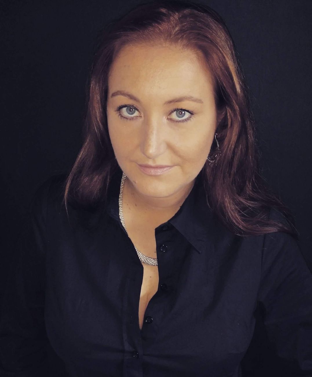 Studioportret van een vrouw in een zwarte blouse met een zilveren ketting tegen een donkere achtergrond.
