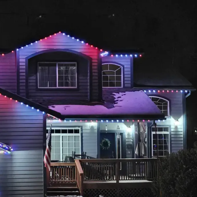House decorated with red, white, and blue lights at night, with snow on the roof and porch.