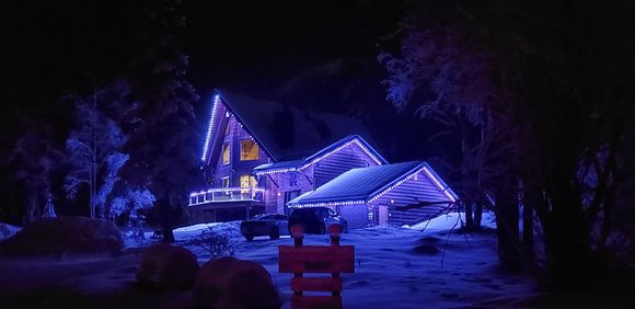 Snowy house lit with blue-purple Christmas lights at night