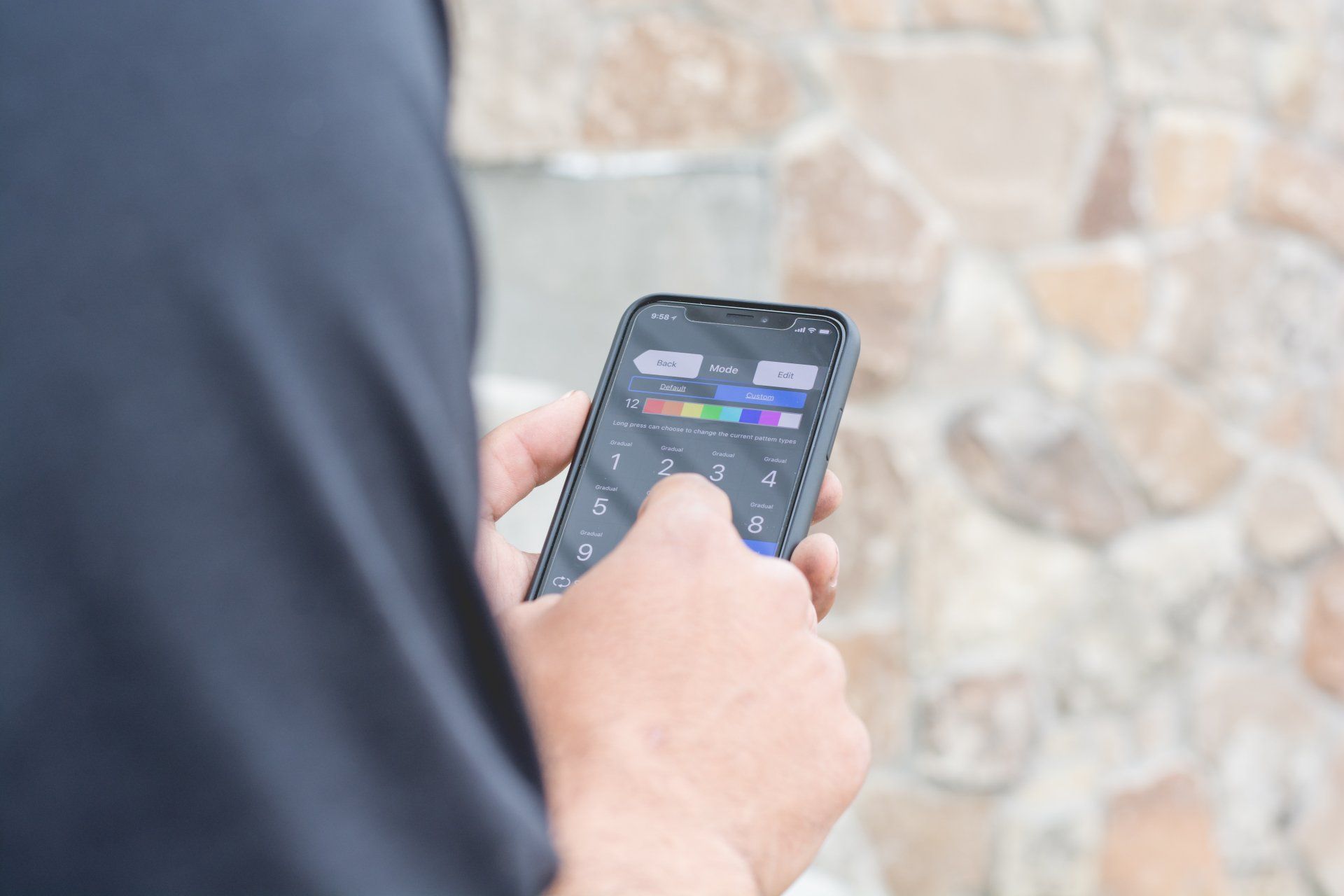 Person using a smartphone with a dark app screen against a stone wall background