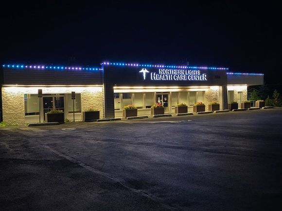 Nighttime exterior of a brick church building with lit windows and a neon sign along an empty parking lot