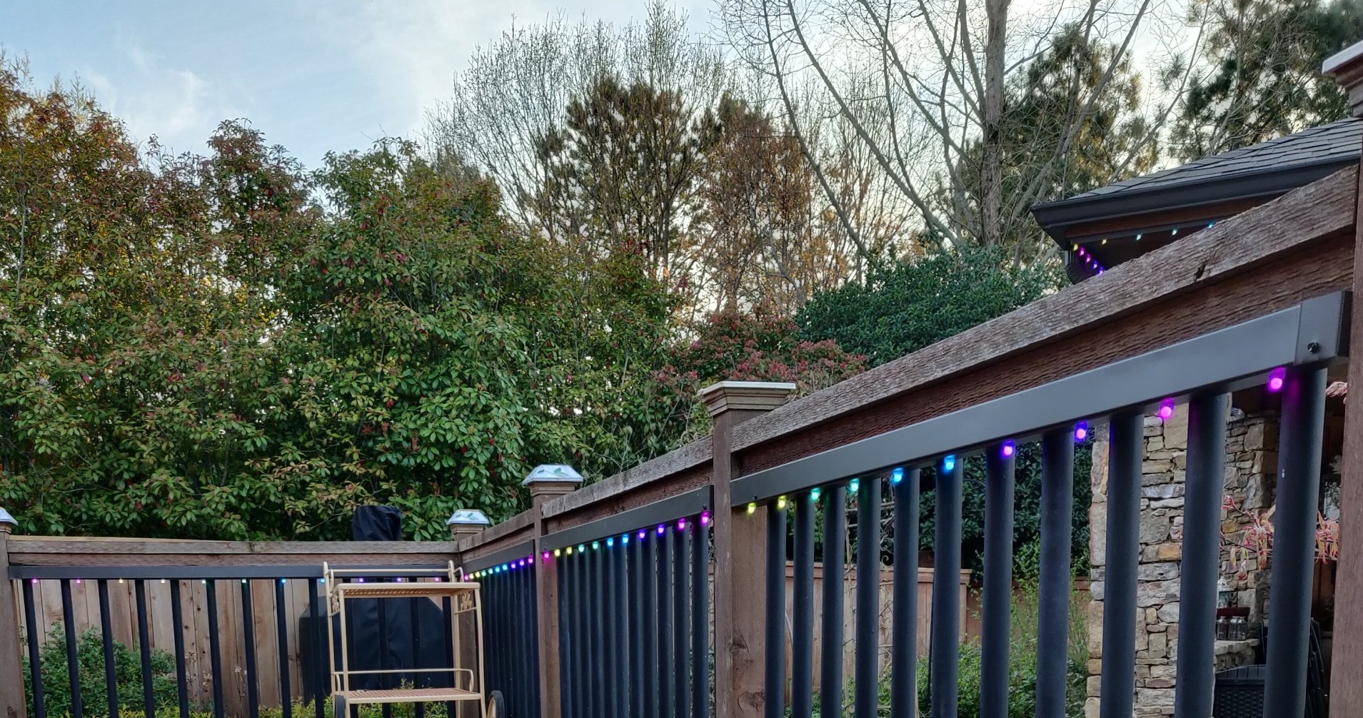 Back deck with railings lined in multicolor string lights, overlooking trees at dusk